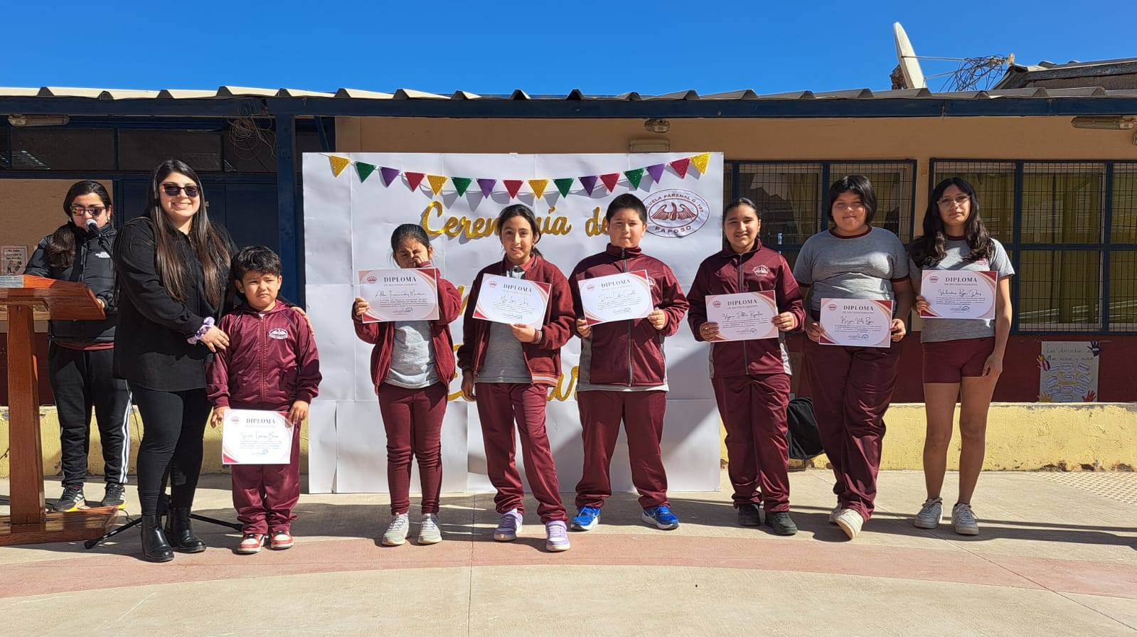Docente y estudiantes de la Escuela de Paposo muestran diplomas frente al lienzo de Ceremonia de Convivencia Escolar