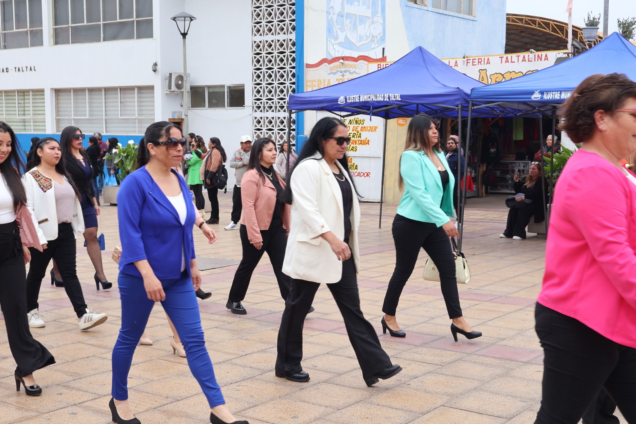 Funcionarias del liceo desfilan frente a carpas municipales en tonos azul y menta.