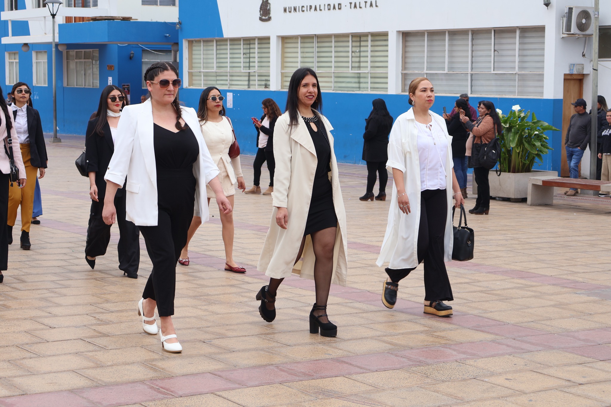 Profesoras con vestimenta clara desfilan elegantemente por la plaza durante la celebración escolar.