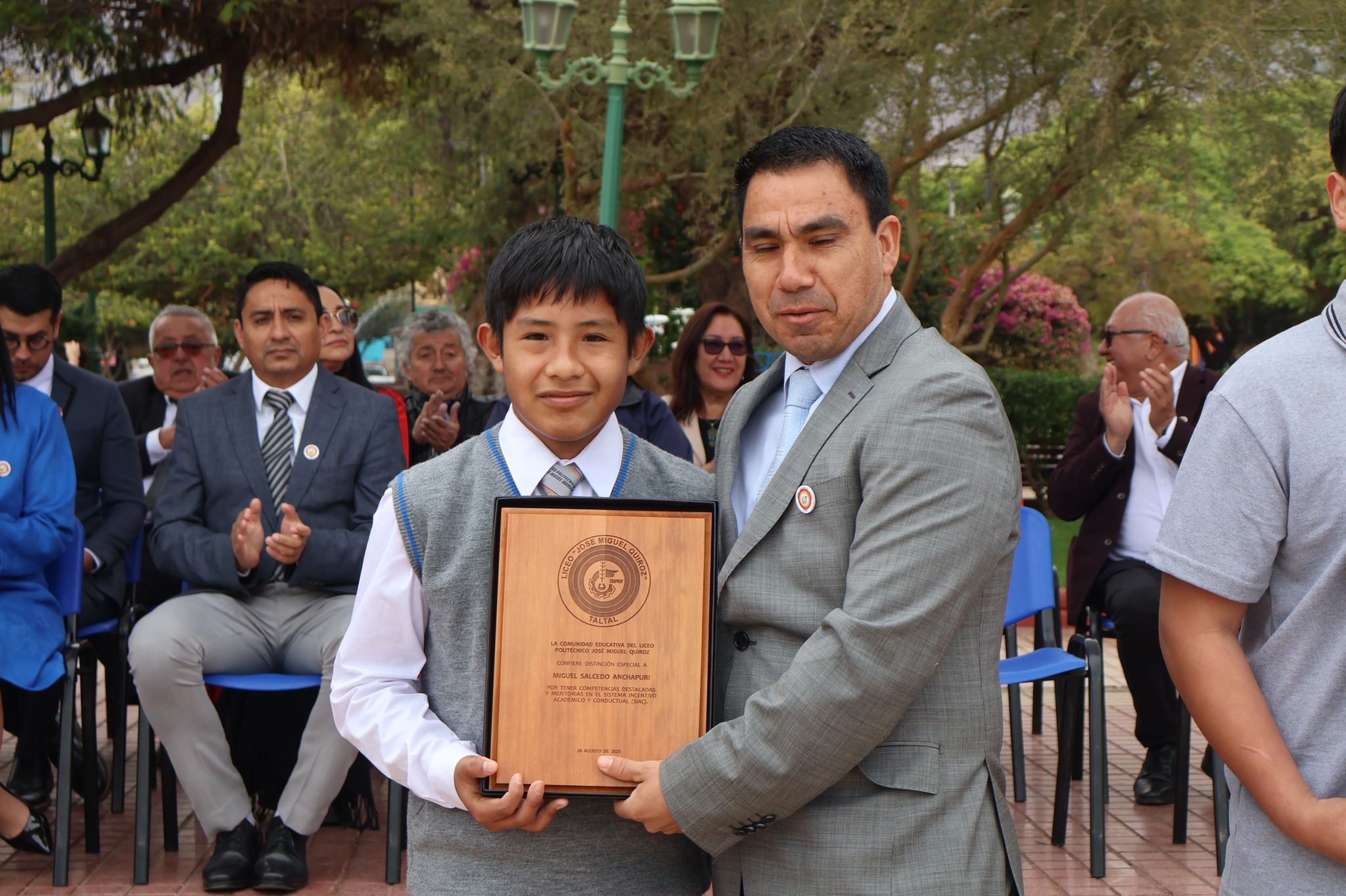 Alumno de enseñanza media posa con galvano junto a directivo durante la ceremonia de premiación.
