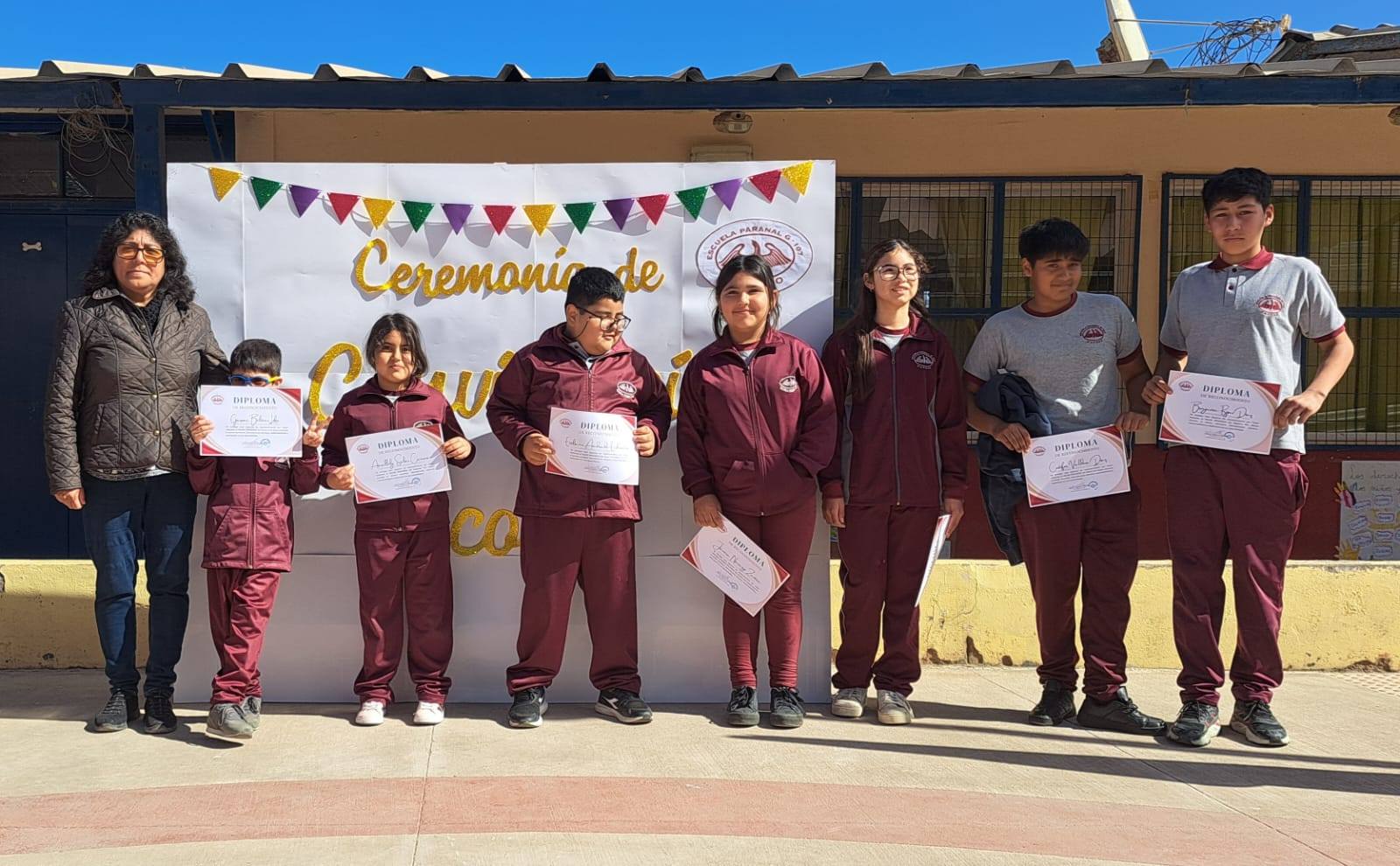 Docente y estudiantes de la Escuela de Paposo muestran diplomas frente al lienzo de Ceremonia de Convivencia Escolar