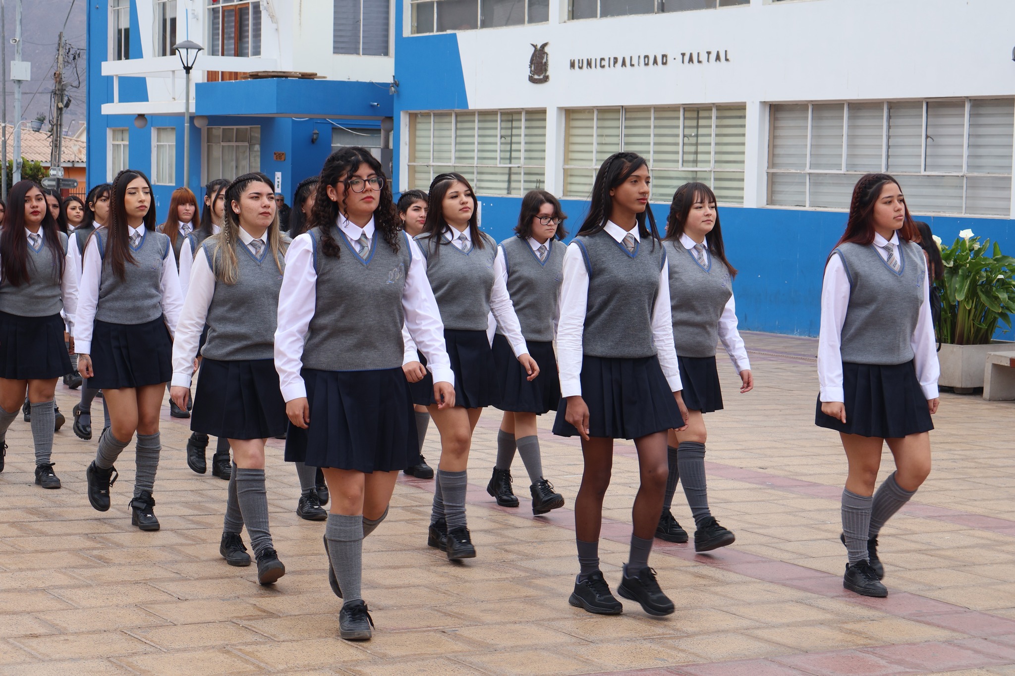 Estudiantes secundarias avanzan en filas uniformadas durante el desfile cívico frente a la municipalidad.