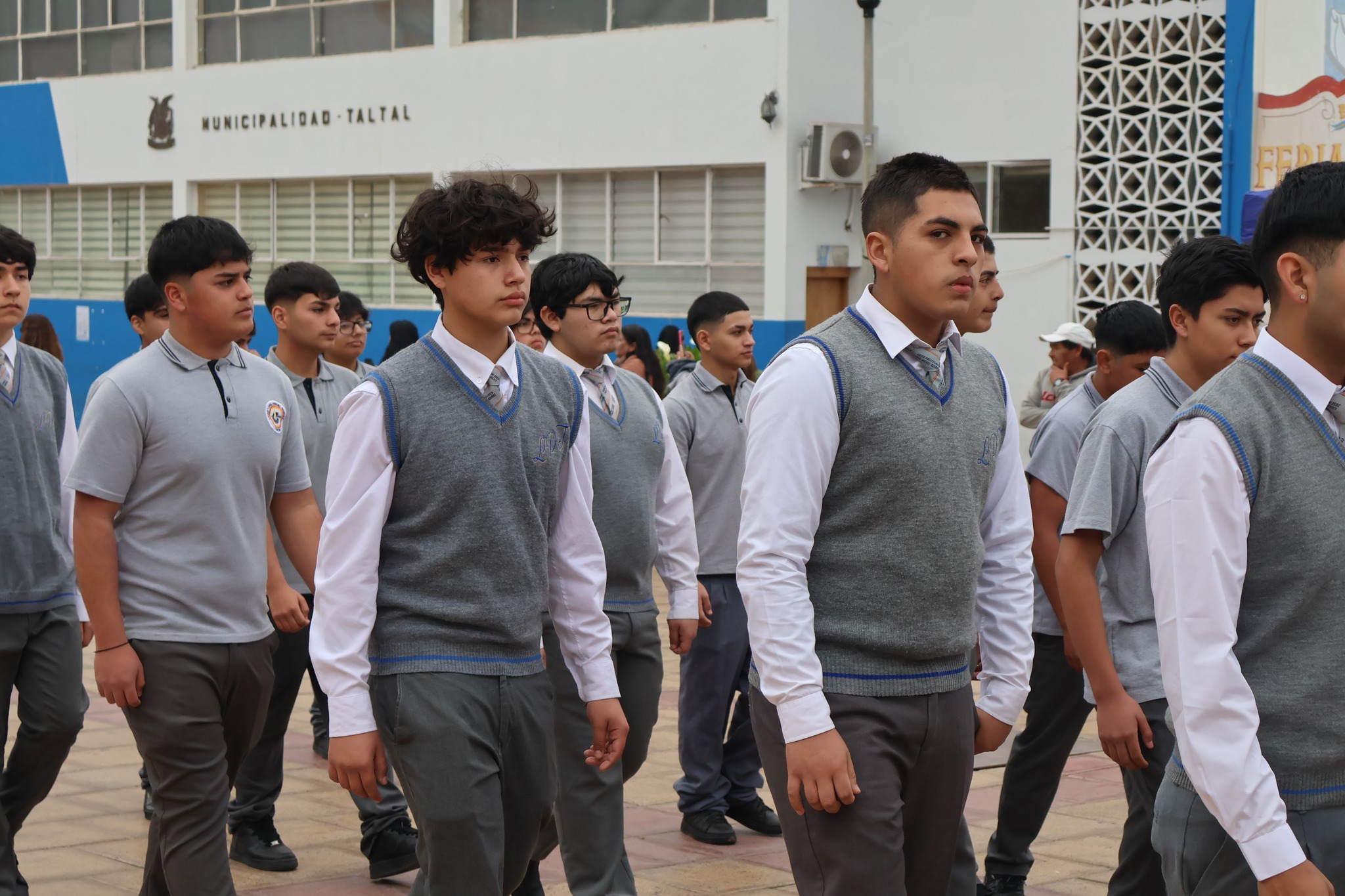 Estudiantes varones con chaleco y corbata grises desfilan frente al municipio de Taltal.