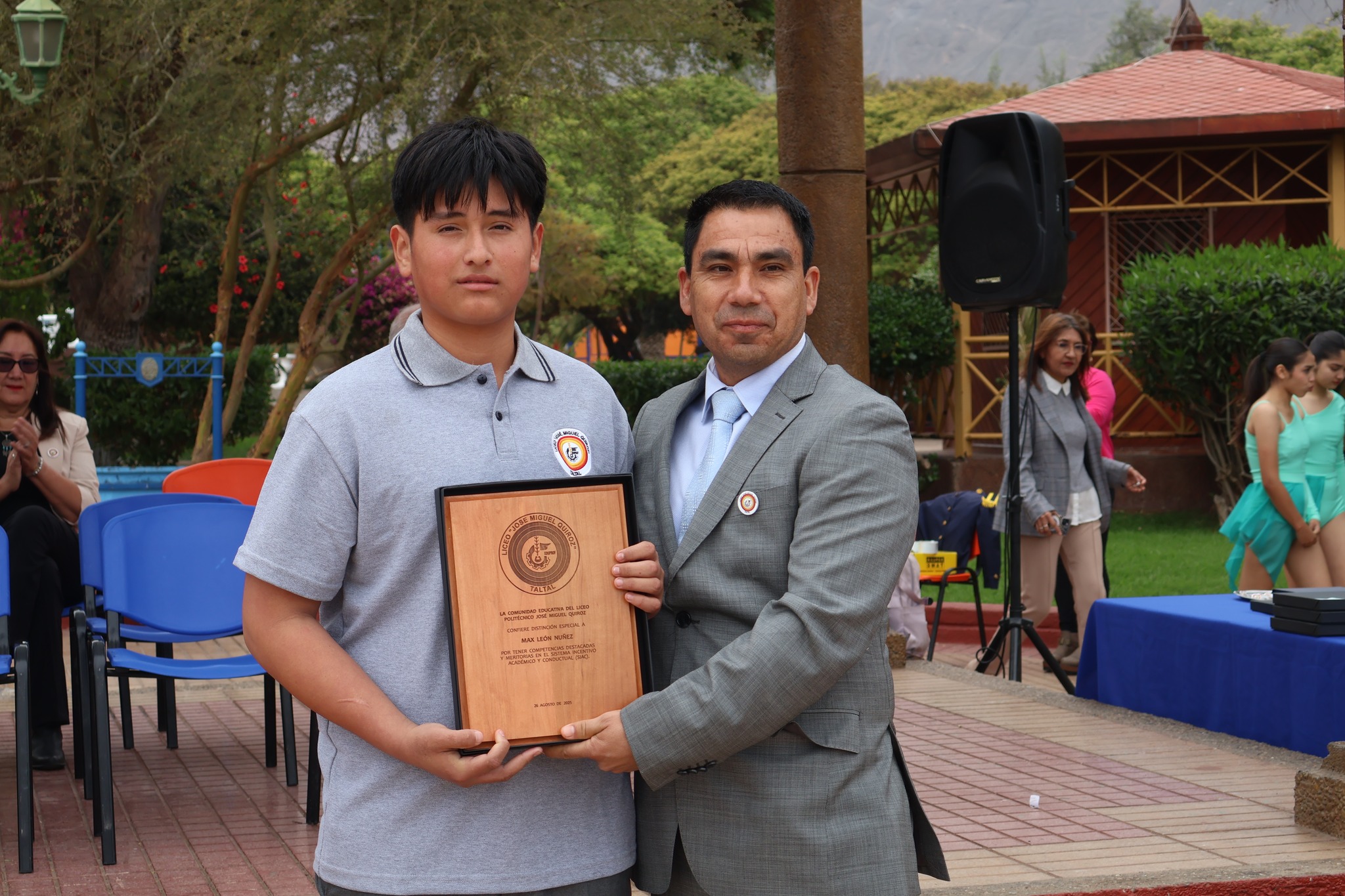 Joven estudiante con polera institucional sostiene reconocimiento por mérito en acto oficial.