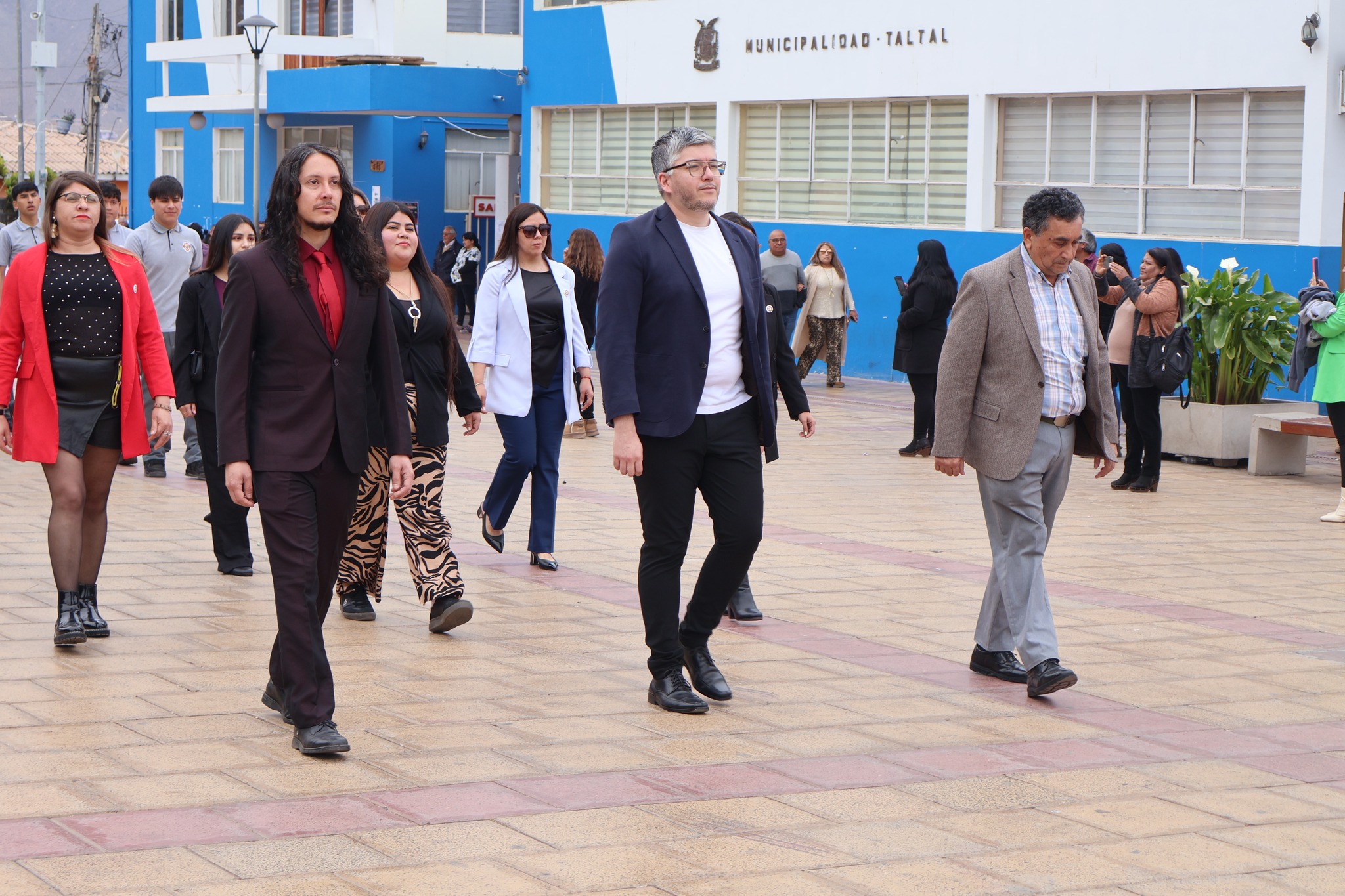 Docentes y asistentes, hombres y mujeres, avanzan ordenadamente durante el acto cívico.