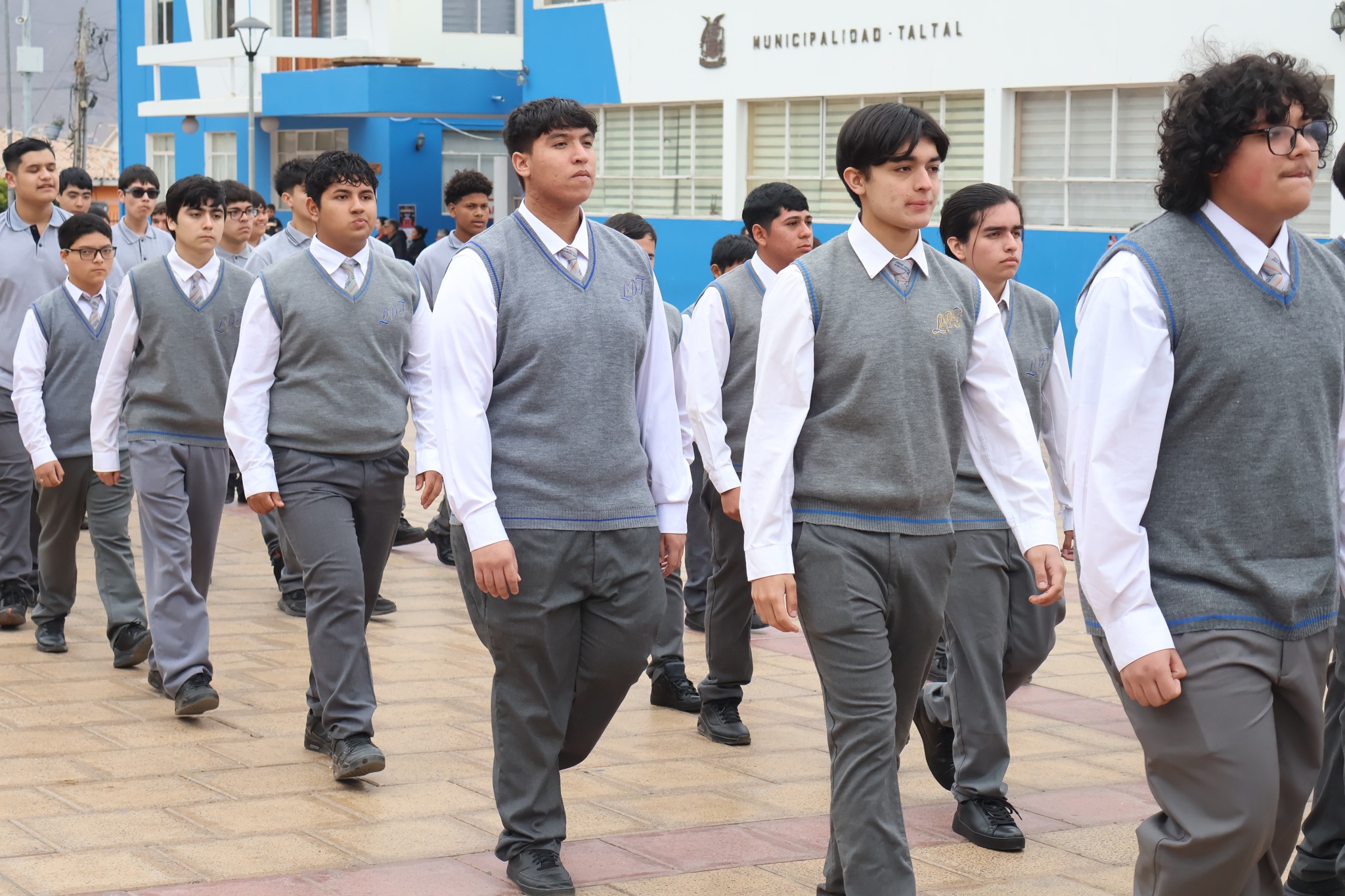 Alumnos de enseñanza media marchan con chalecos grises y camisa blanca en el desfile del Liceo Politécnico.