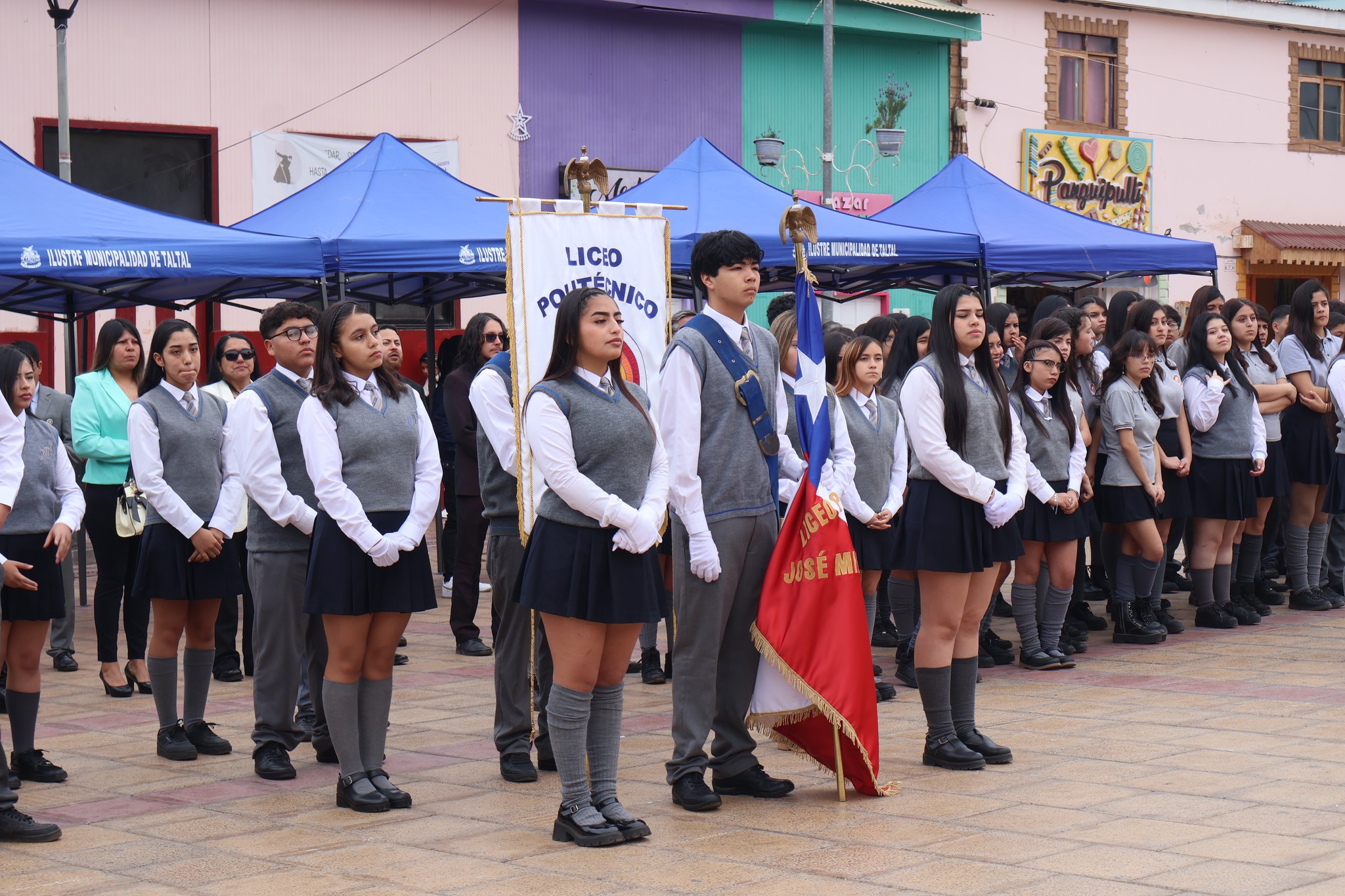 Delegación estudiantil con estandarte y bandera del Liceo José Miguel Quiroz lista para el desfile aniversario en la plaza.