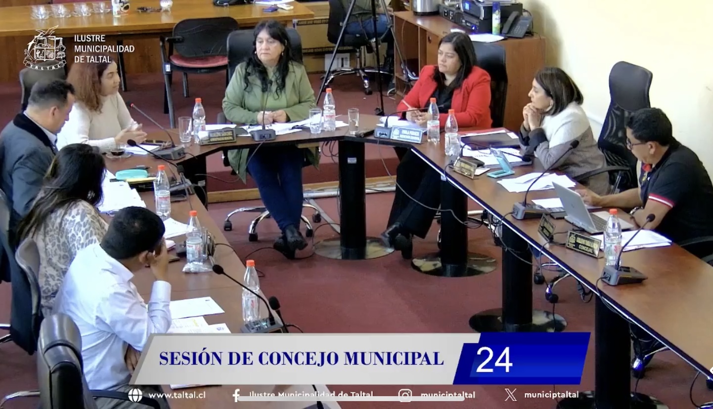 concejo-taltal-sesion-24-becas-paranal-pasantia-tacna-seguridad-19-08-2025-pulsocomunal Concejales de Taltal en sesión ordinaria; dos ediles conversan frente a micrófonos en sala municipal de madera