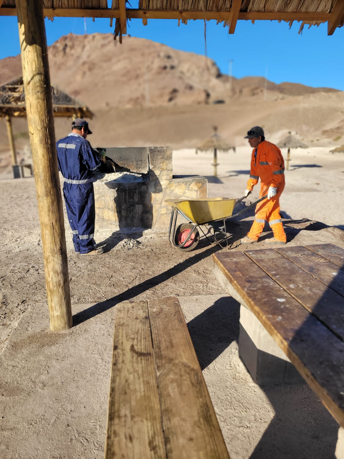 Detalle de mantenimiento: funcionarios limpian la parrilla del quincho con carretilla y herramientas en Muelle de Piedra.