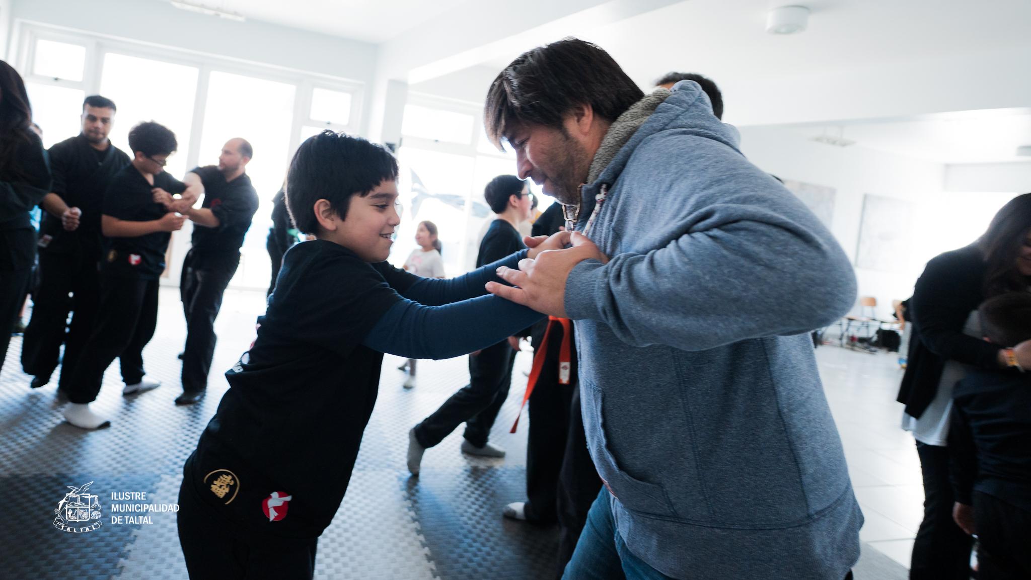 Práctica de defensa personal con control de muñeca entre dos participantes, con público observando en Taltal.