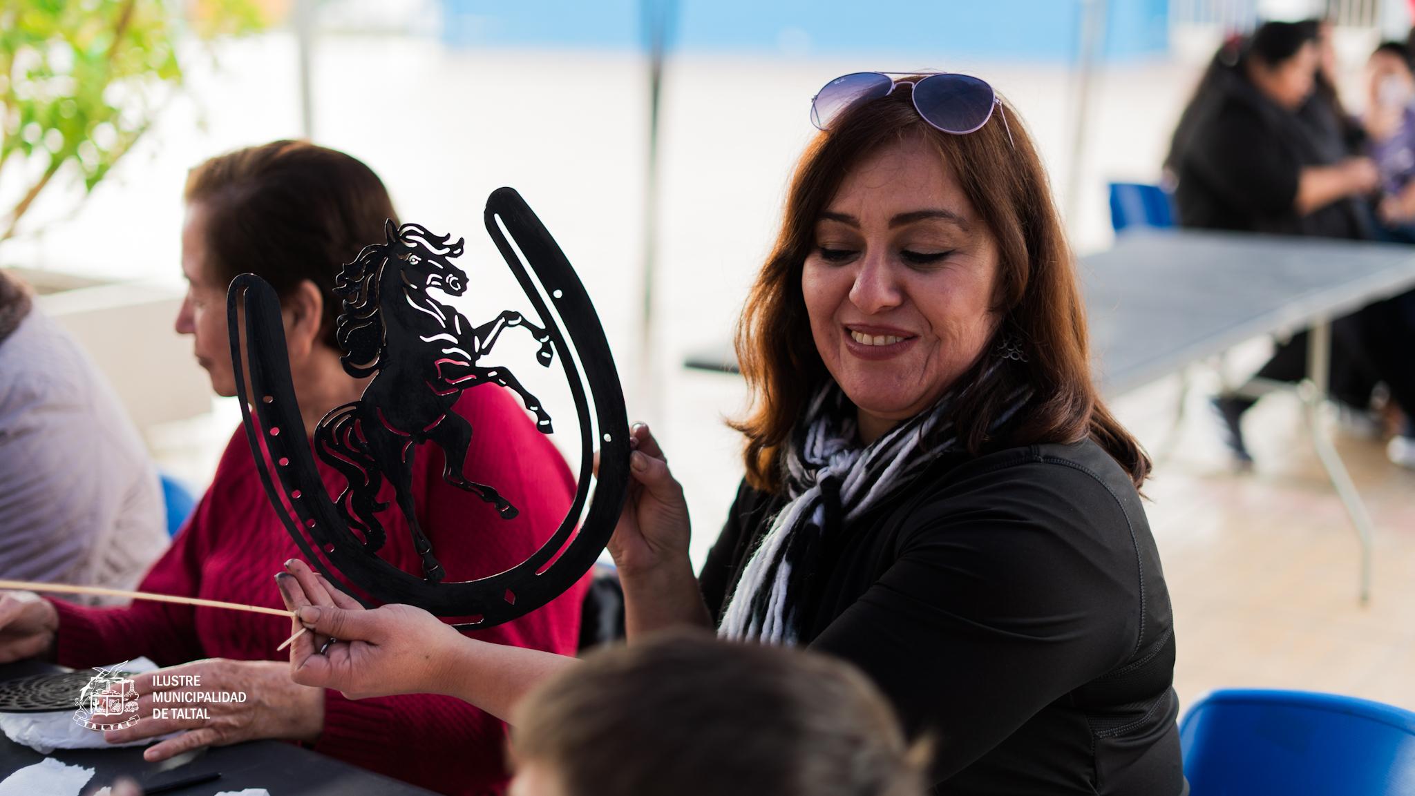 Participante sostiene artesania de herradura con silueta de caballo en taller comunitario.