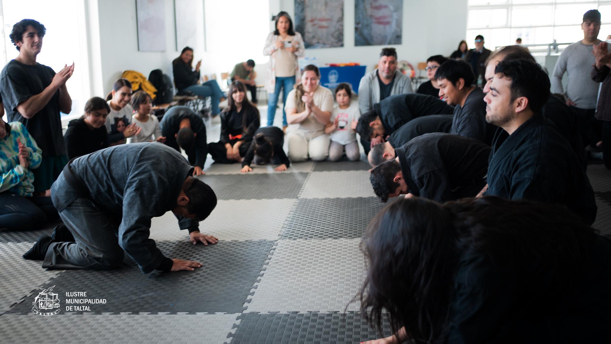 Practicantes realizan el saludo tradicional inclinándose en el tatami mientras familias aplauden el encuentro de artes marciales en Taltal