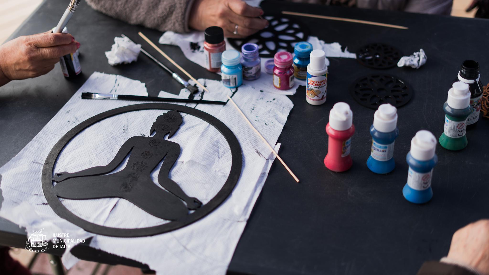 Mesa con pinceles y pinturas junto a figuras caladas usadas en el taller.