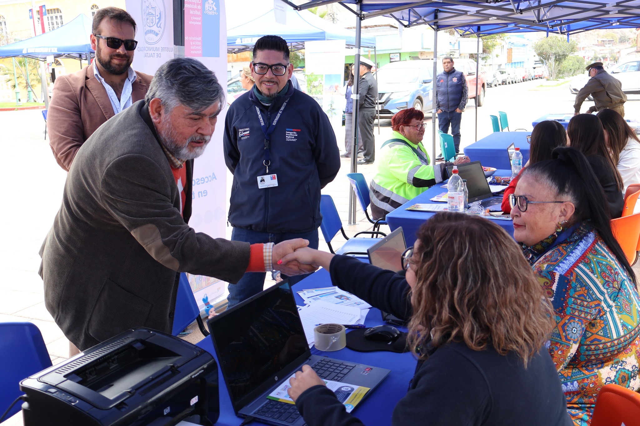 Alcalde (s) saluda a usuaria en mesa de atención ciudadana durante la feria de servicios.