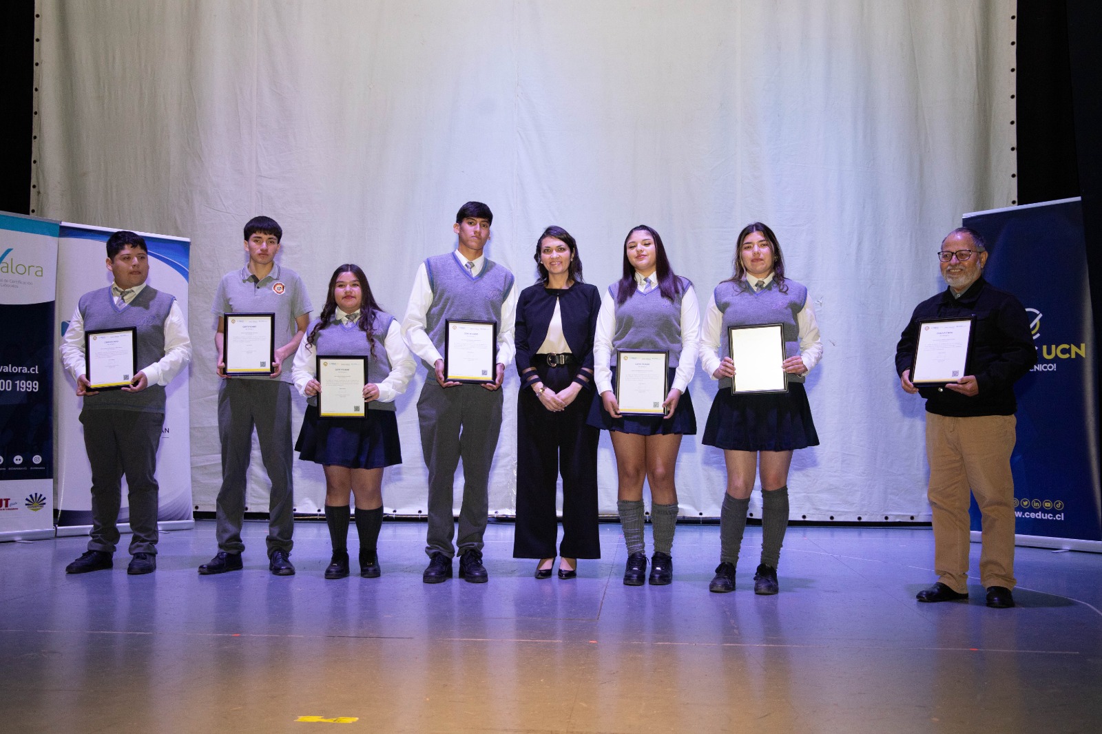 Grupo de estudiantes certificados posa con sus actas frente a pendones de CEDUC UCN e Impronta Mine.