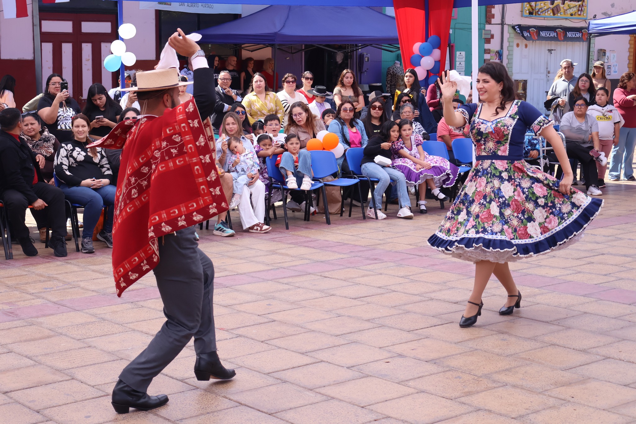 Jurado realiza una demostración en la cuca, levantando el pañuelo, con vestido floreado ante el público en la Plaza Arturo Prat de Taltal durante el Campeonato Comunal 2025.
