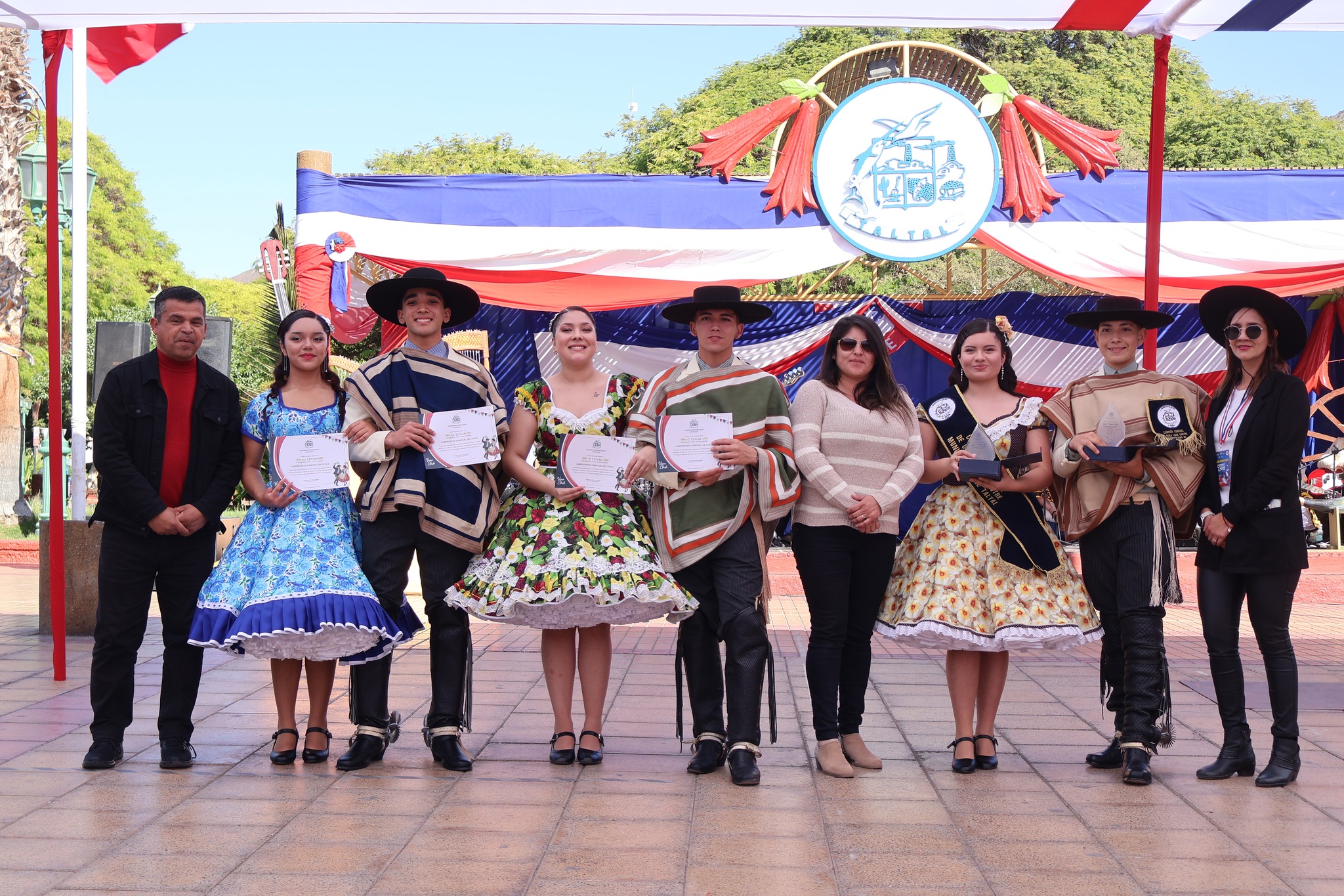 Estudiantes de enseñanza media son destacados en el podio del comunal de cueca 2025, junto a autoridades y banda en el escenario.
