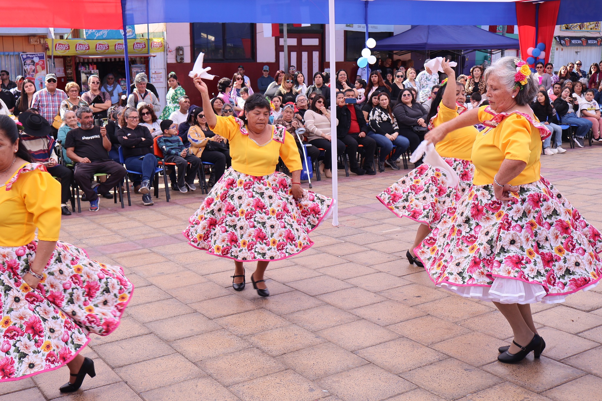 Agrupación Danzas Doradas en escena: adultas mayores con blusas amarillas y faldas florals interpretan cueca con pañuelos.