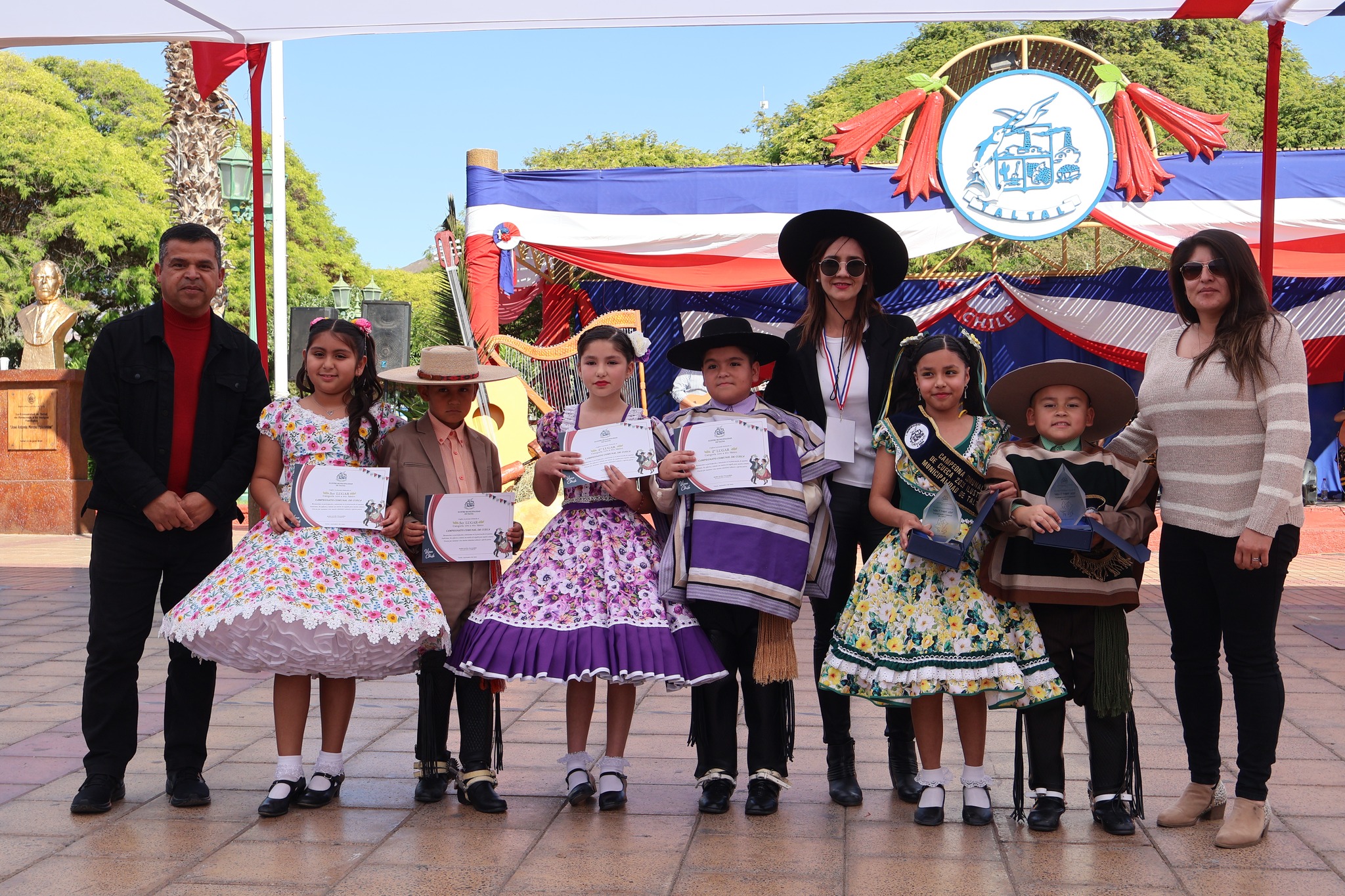 Premiación infantil del Campeonato Comunal de Cueca en la Plaza Arturo Prat: niñas y niños con trajes huasos posan con diplomas y trofeos junto a autoridades