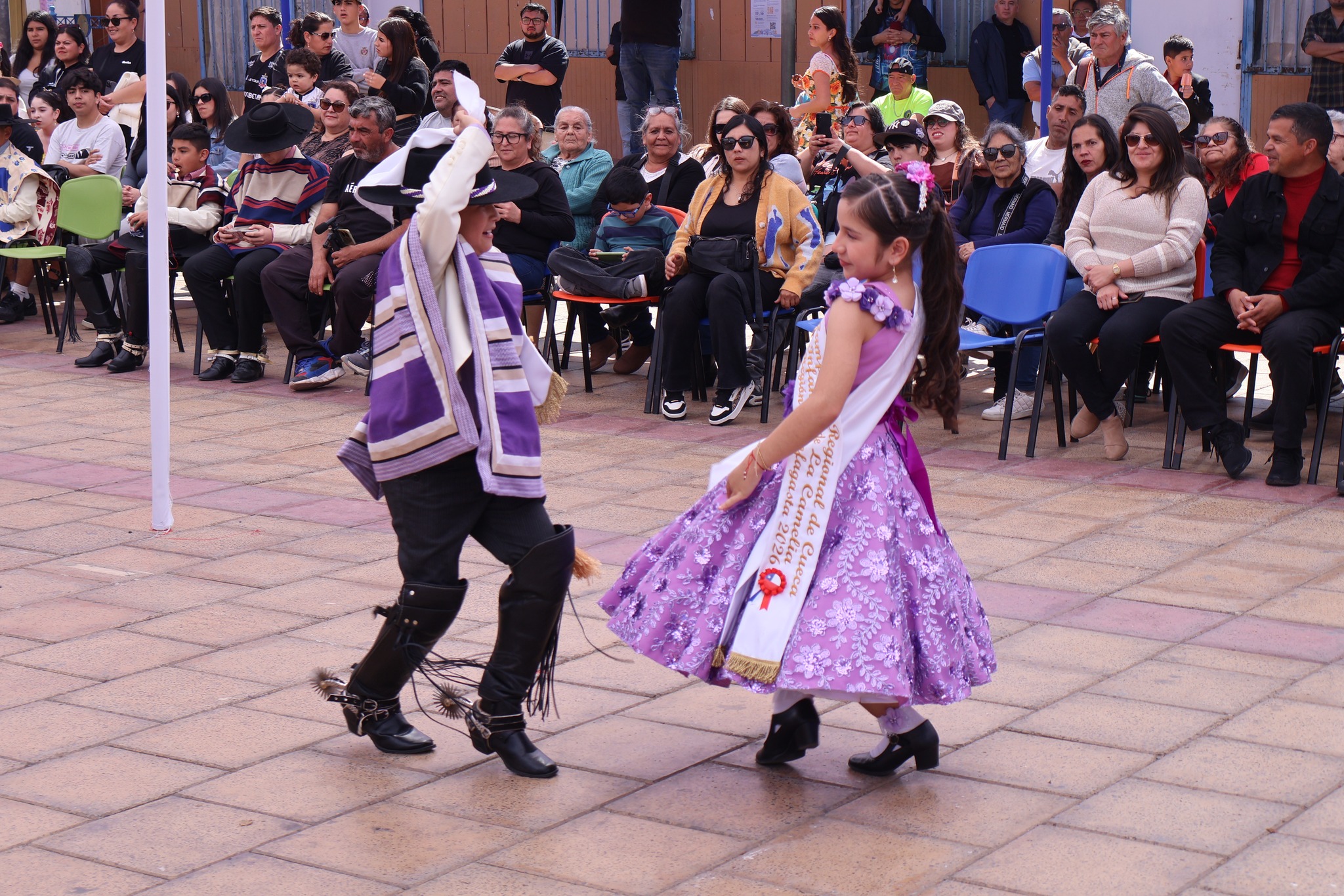 Pareja infantil cont rajes morados baila cueca; la niña luce banda y vestido lila, el niño con manta y espuelas, en el Campeonato Comunal de Cueca de Taltal 2025.