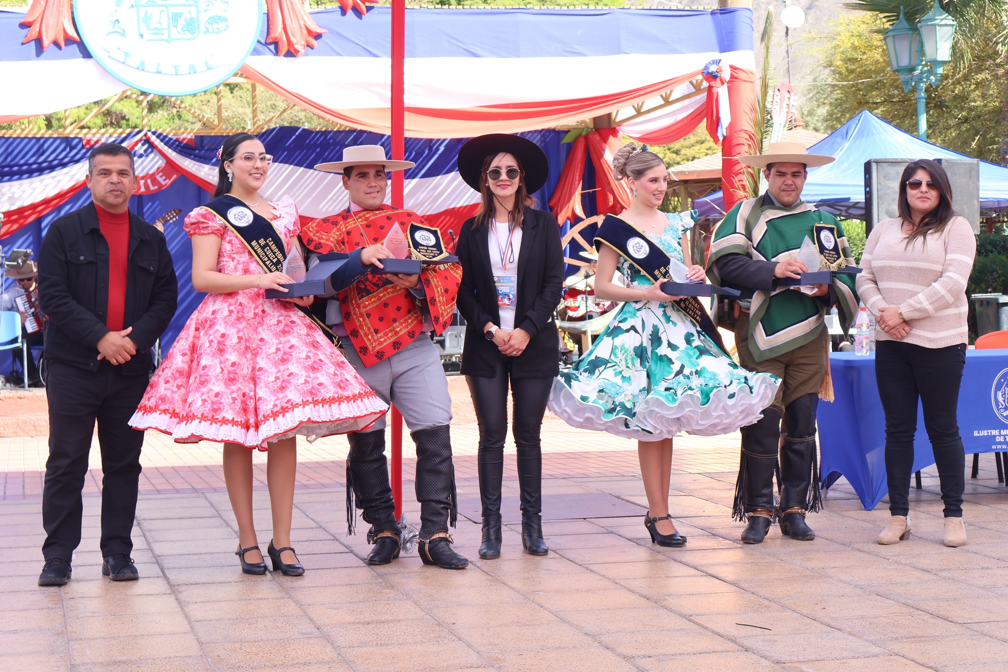Campeones comunales posan con trofeos y bandas en el escenario principal del campeonato, autoridades acompañan la fotografía.