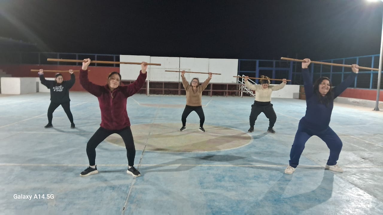 Vecinas de Paposo participan en clase de actividad física nocturna con palos de entrenamiento en la multicancha.