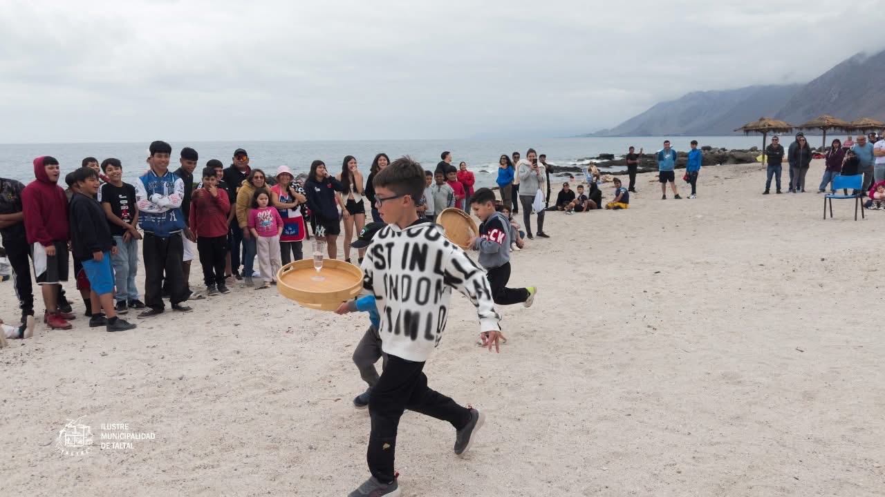 Carrera del mozo infantil con bandejas y vasos frente al público en la playa.
