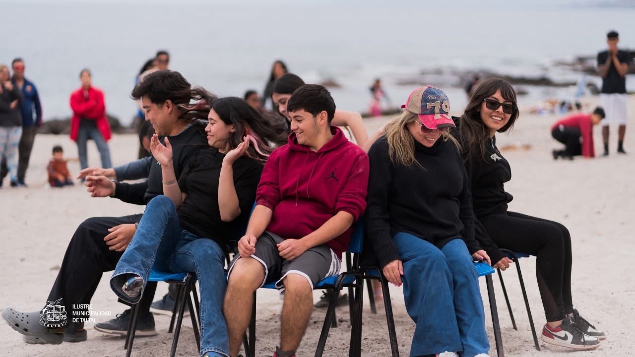 Jóvenes y adultos jugando a la silla musical en la playa de Poza Las Peñas.