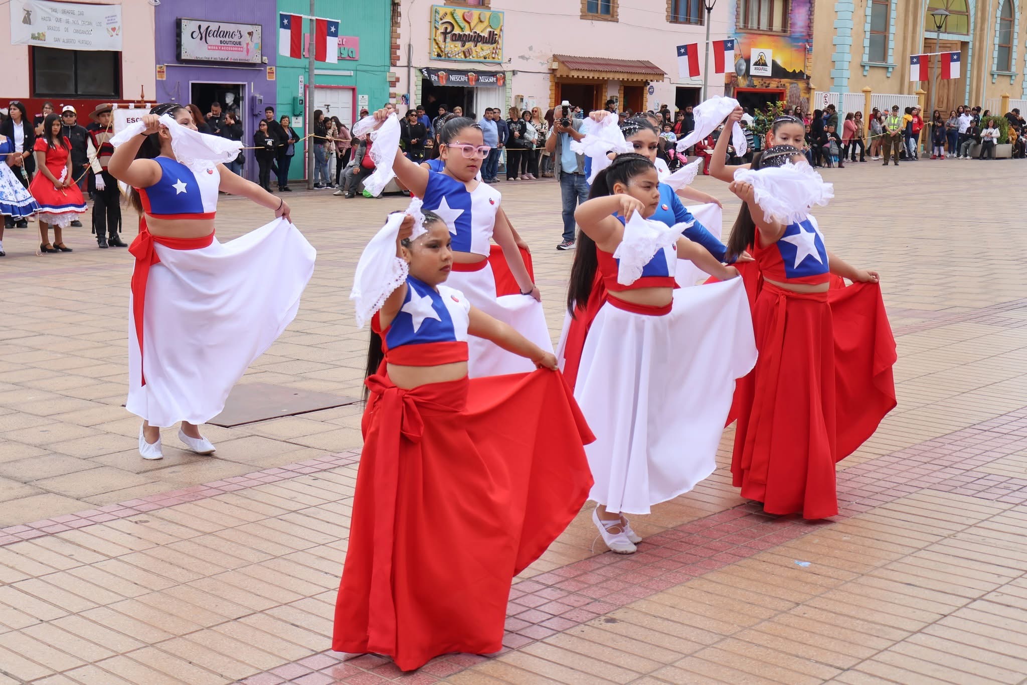Niñas con trajes rojo, blanco y azul bailan con pañuelos en plaza de Taltal.
