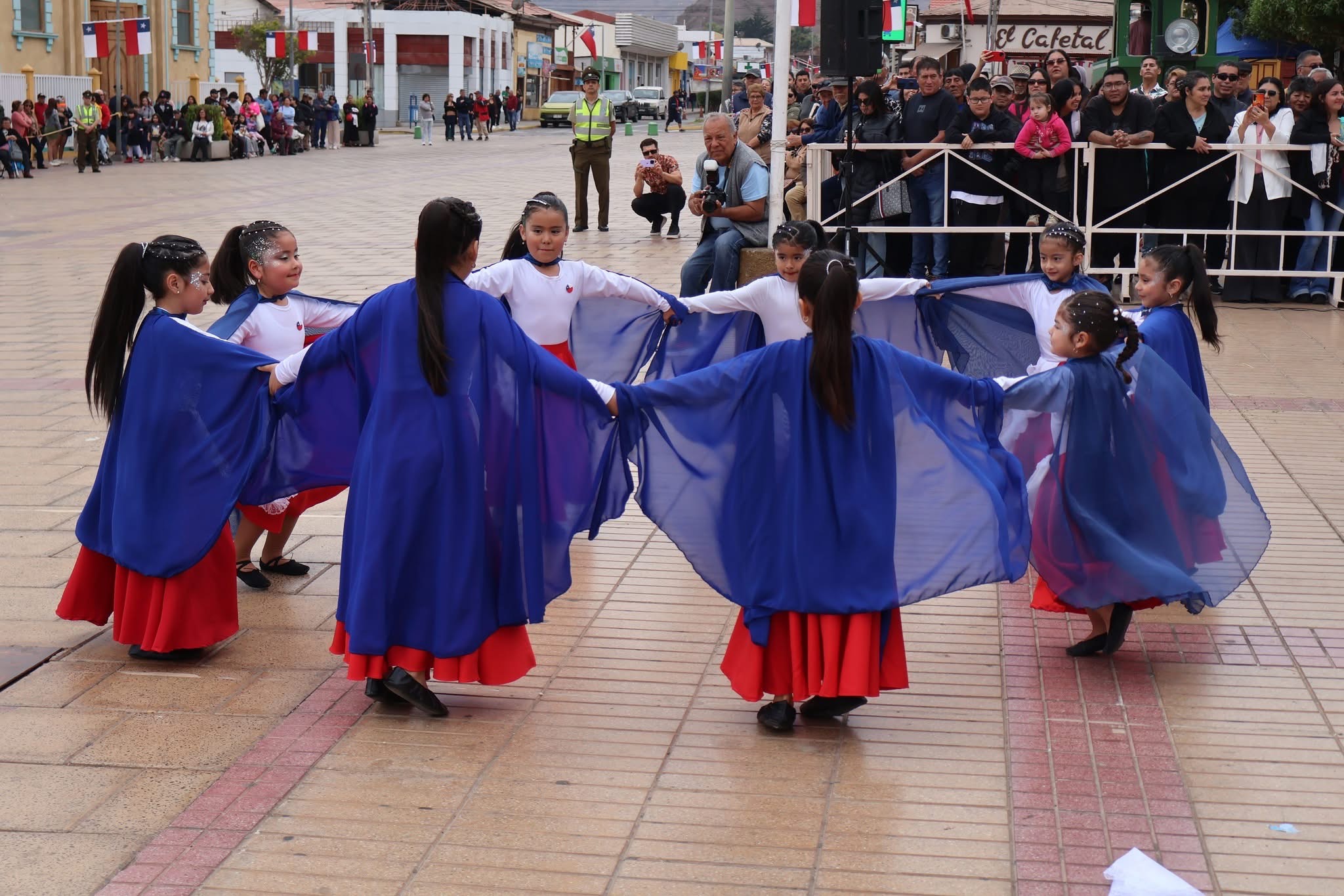 Rueda de niñas con capas azules realiza una danza folclórica frente al público