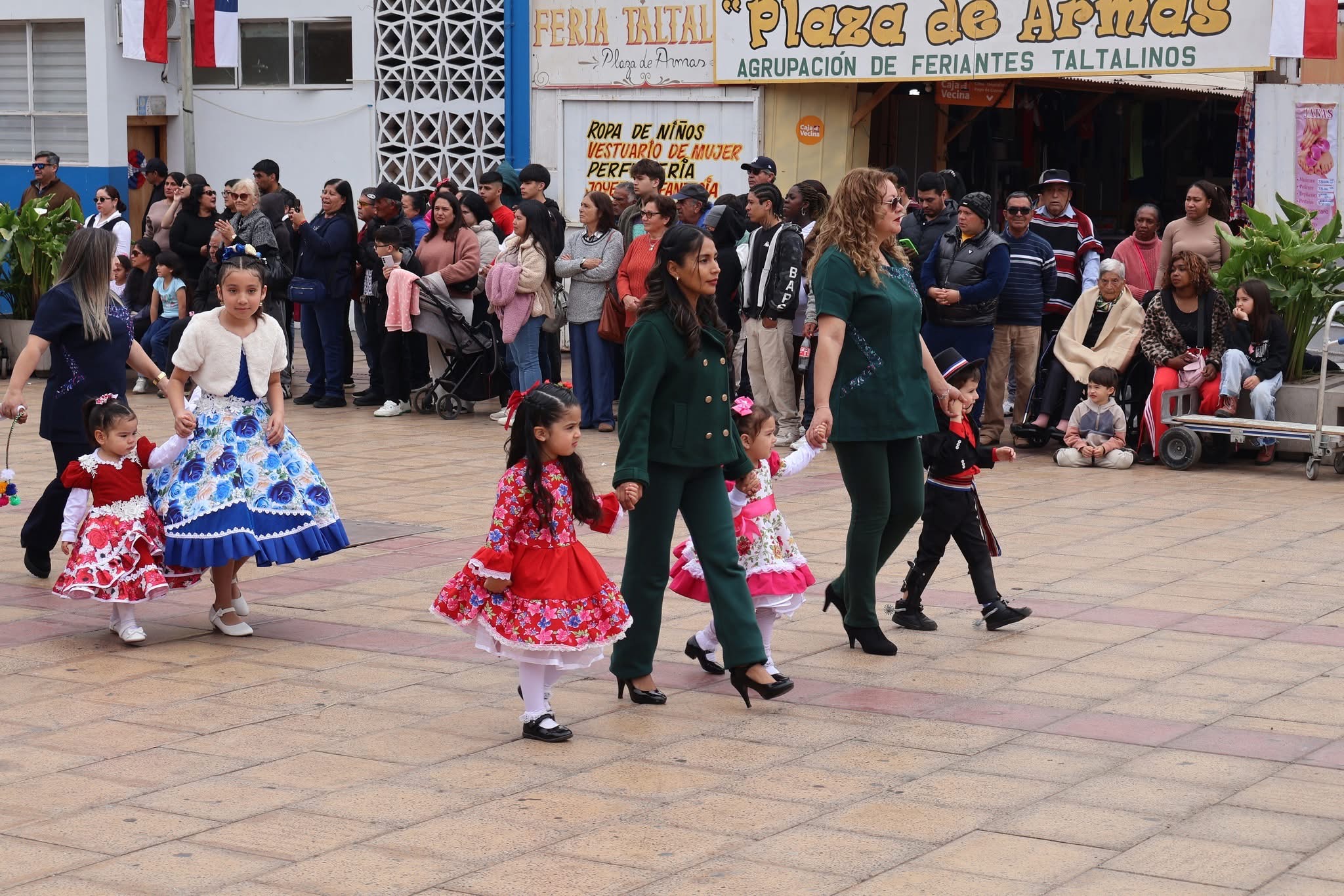 Educadoras guían a niñas con vestidos florales de huasa en el desfile de Fiestas Patrias en Taltal.