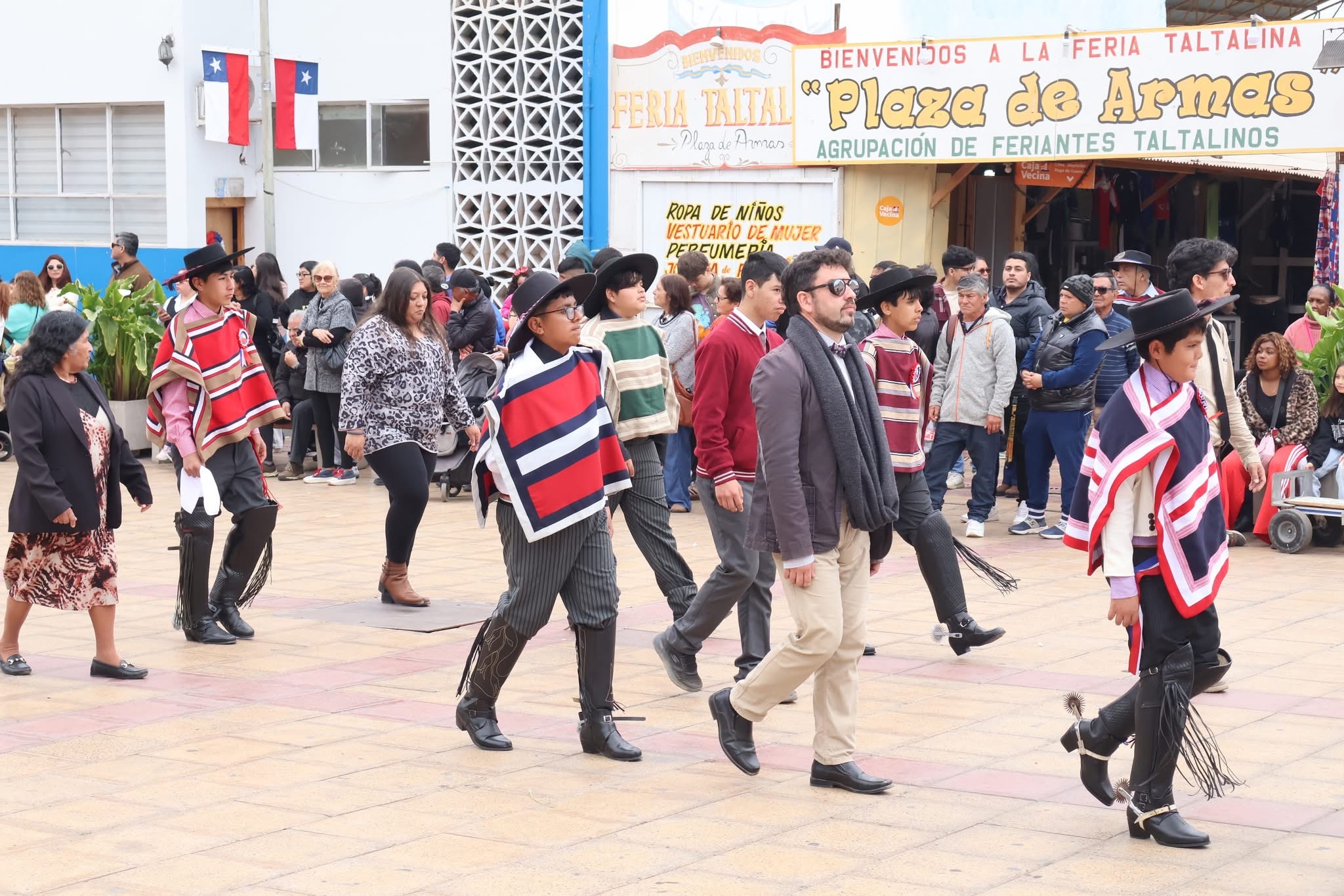 Estudiantes marchan con mantas y sombrero de huaso, acompañados por docente, en el desfile de Fiestas Patrias de Taltal.