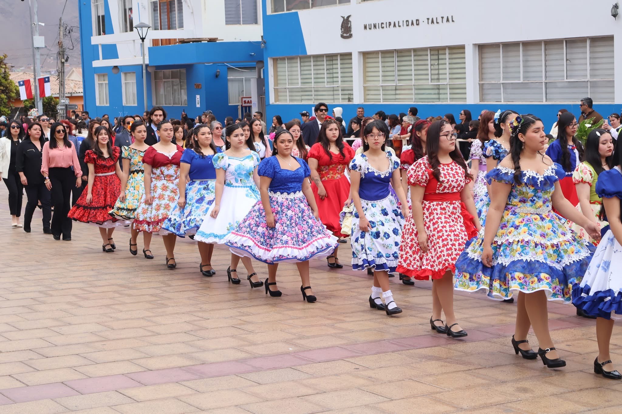 Gran bloque de alumnas con vestidos florales y profesores al fondo participan del desfile dieciochero en el centro de Taltal.