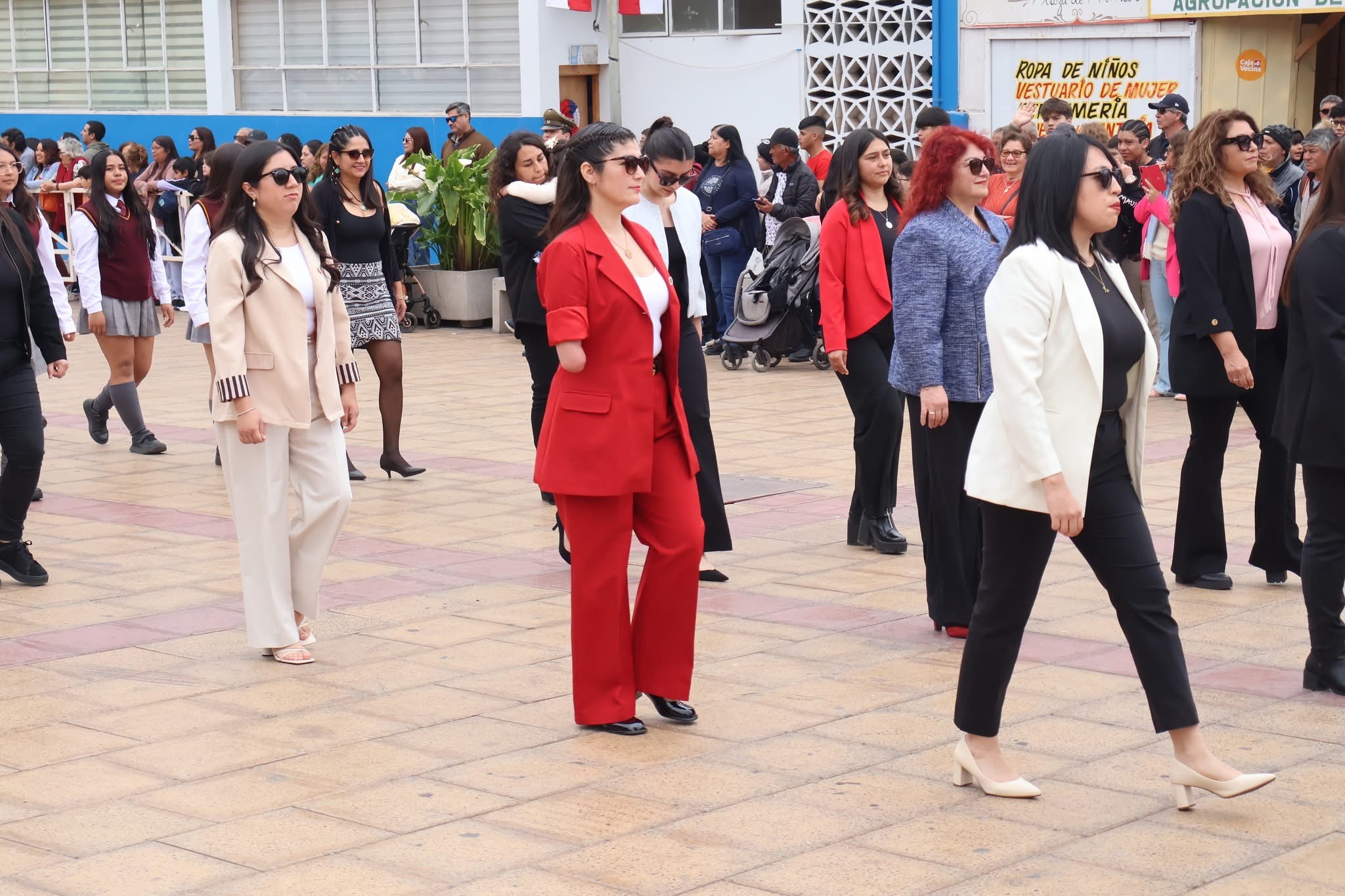 Comitiva de mujeres con vestimenta formal en tonos rojos, blanco y negro desfila por la Plaza de Armas de Taltal.