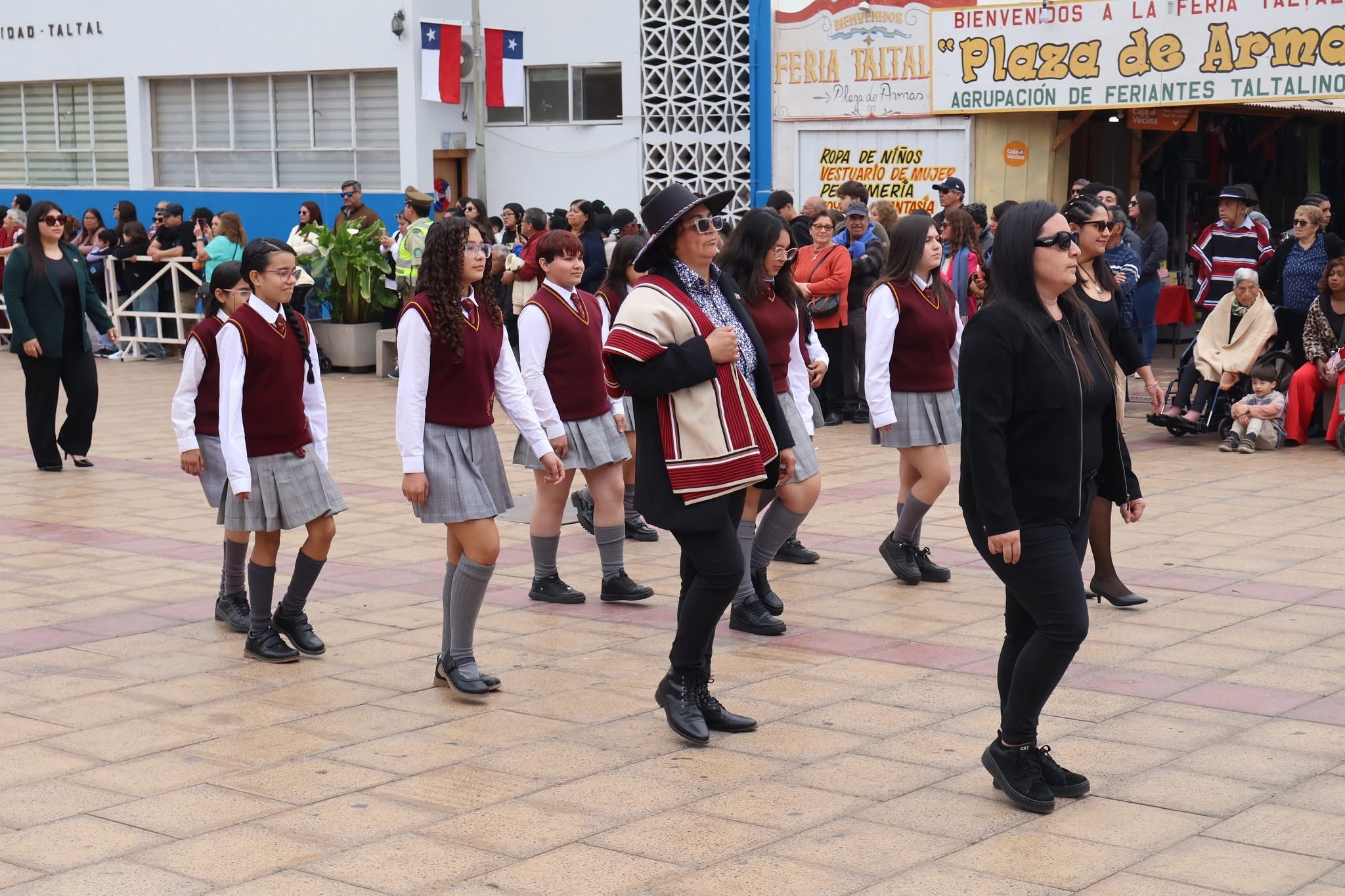 Estudiantes con uniforme burdeos y gris marchan junto a sus profesoras durante el desfile de Fiestas Patrias en Taltal.