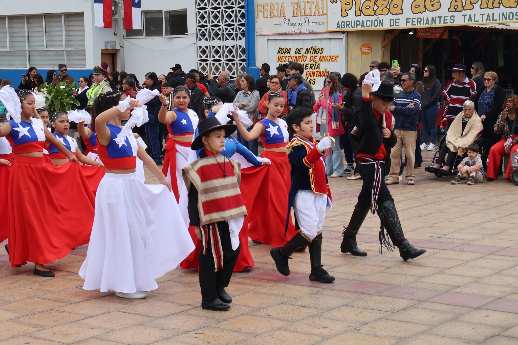 Niñas con faldas rojas y blancas con estrella azul y niños con vestimenta de huaso y traje histórico desfilan en la Plaza de Armas de Taltal.
