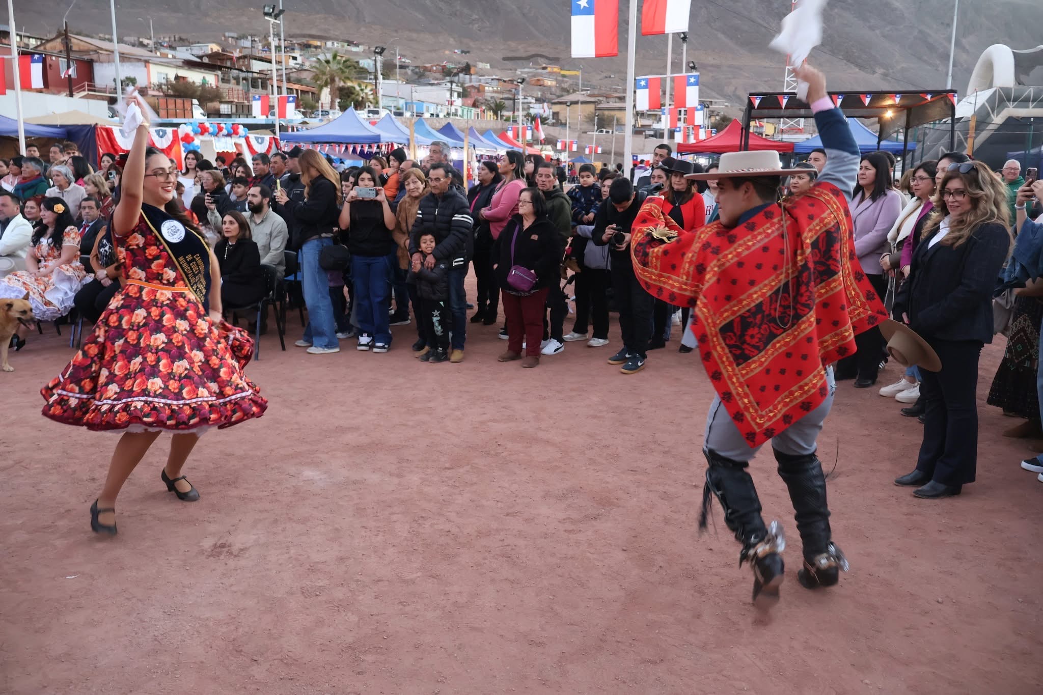 Pareja campeona comunal de cueca se presenta ante el público, luciendo traje típico y pañuelo alto en la pista principal de las ramadas.