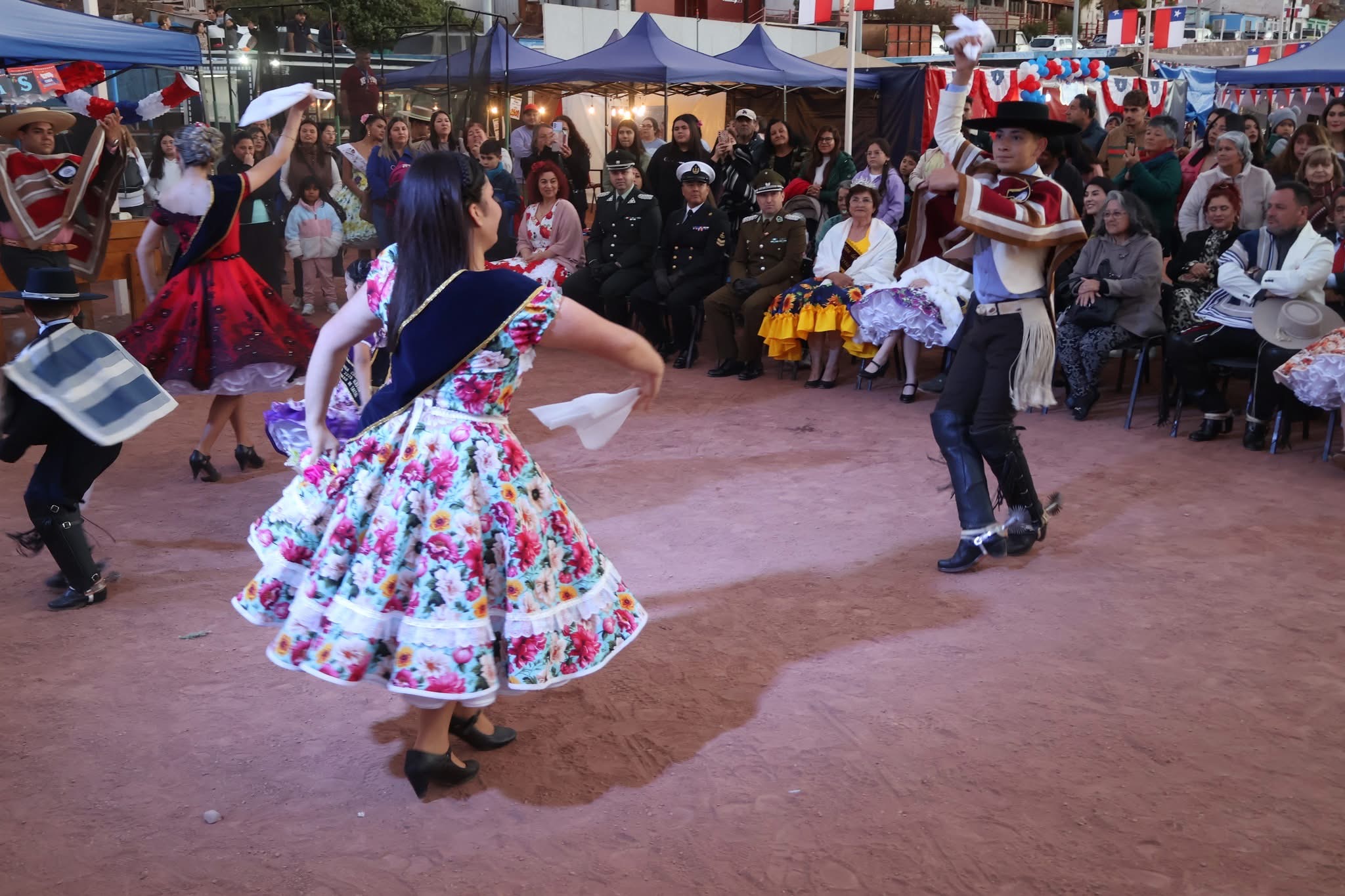 Competidores de distintas muestran su coreografía de cueca en el escenario de tierra, con los stands y autoridades como marco.
