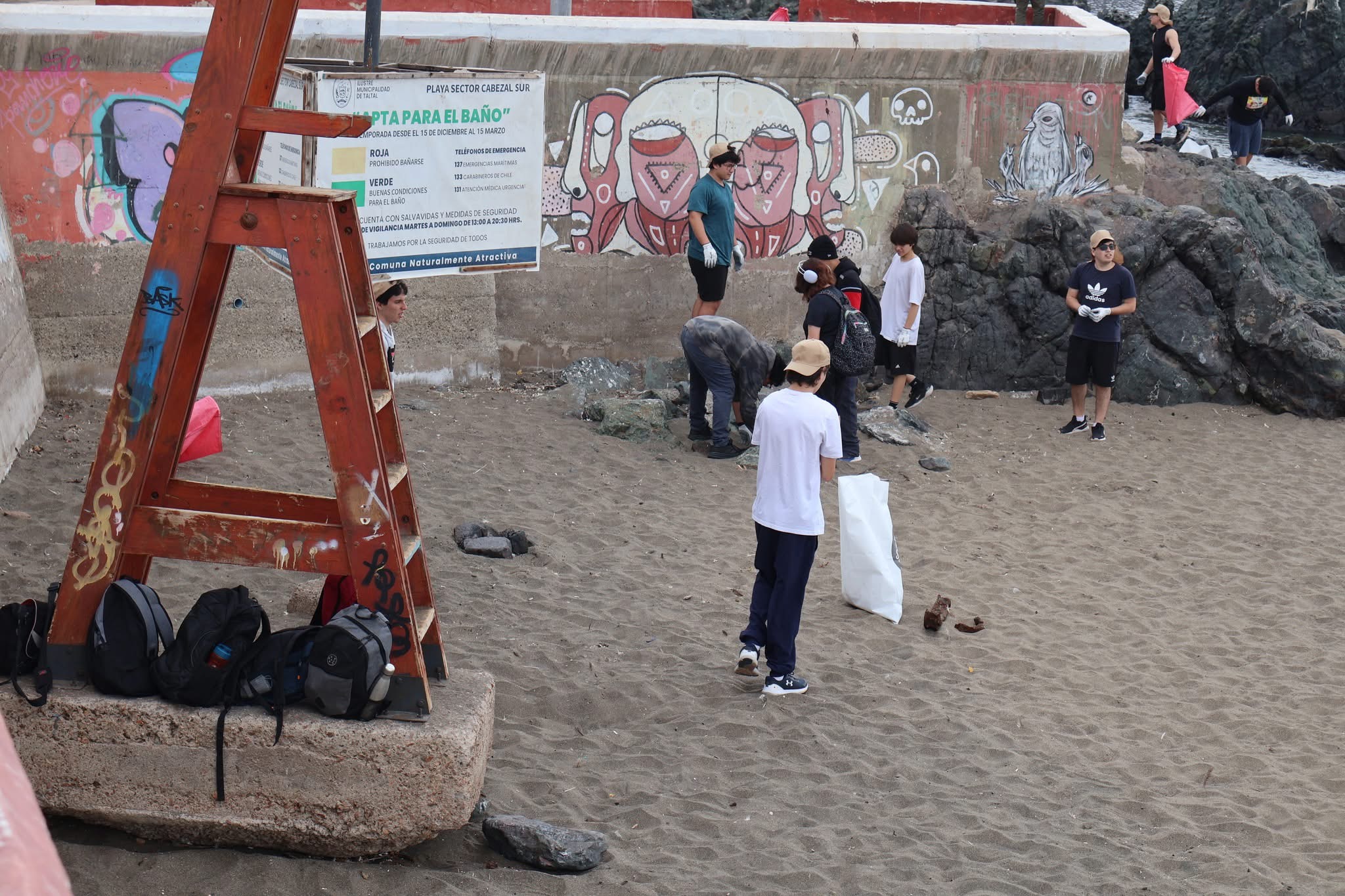 Grupo de jóvenes recogiendo basura junto a murales en la playa Cabezal Sur de Taltal.