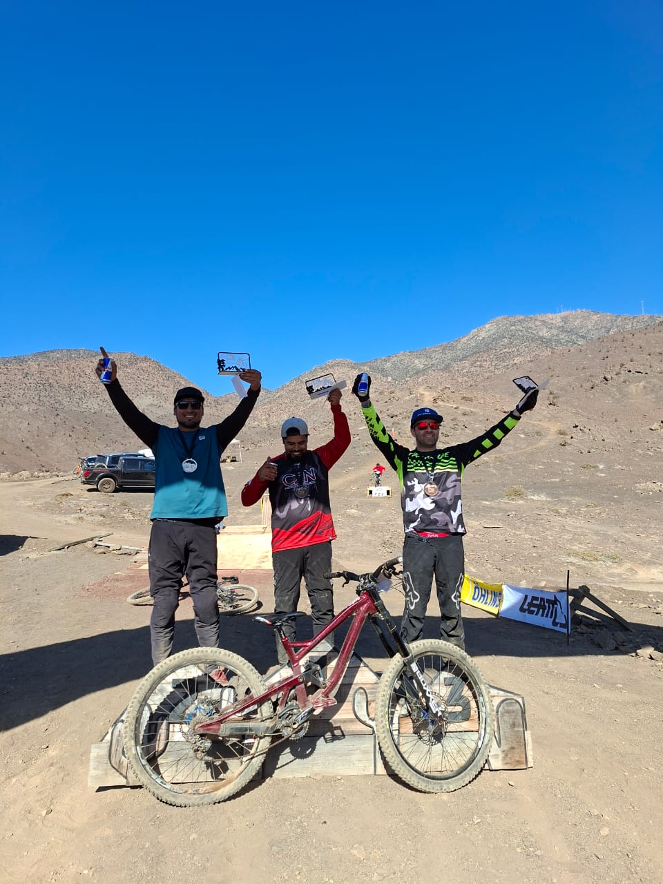Ganadores del Downhill Zonal Norte celebran en el podio con sus bicicletas en Taltal, tras una intensa jornada deportiva.
