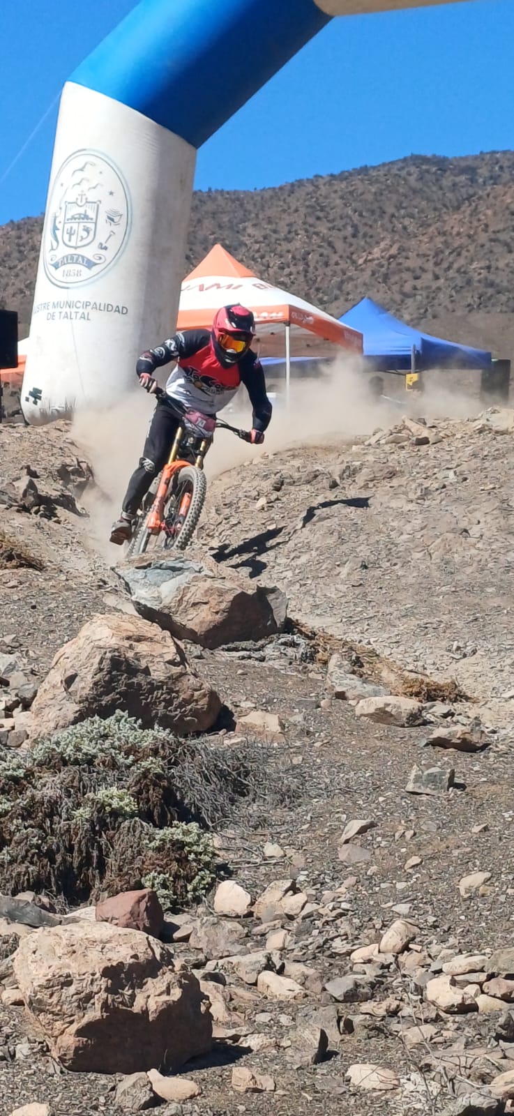 Rider desciende entre rocas y polvo en la partida del Downhill Zonal Norte, bajo el arco de la Municipalidad de Taltal.