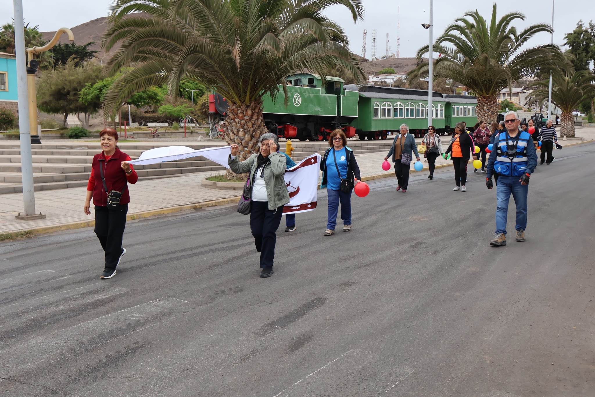 Grupo de participantes marchando sosteniendo una bandera comunitaria y globos de colores.
