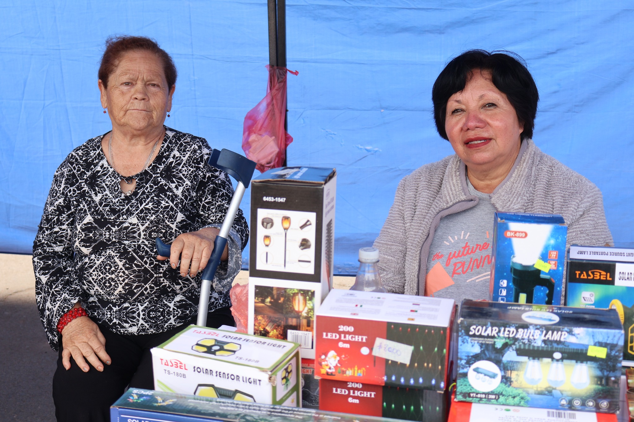 Expositoras taltalinas ofrecen productos de iluminación solar y artículos del hogar en la feria local.