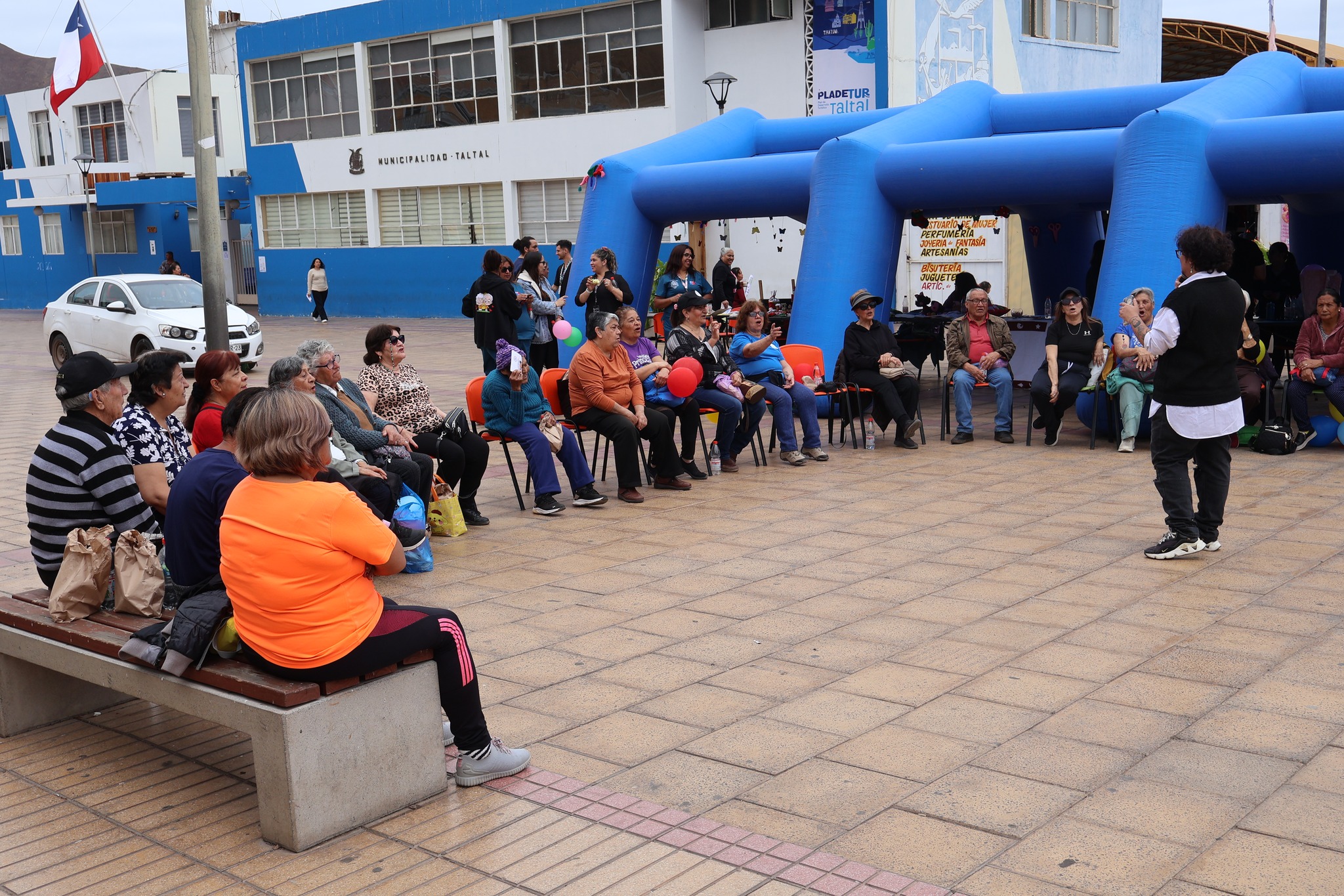 Grupo de adultos mayores sentados en sillas y bancas recibiendo una charla o presentación.