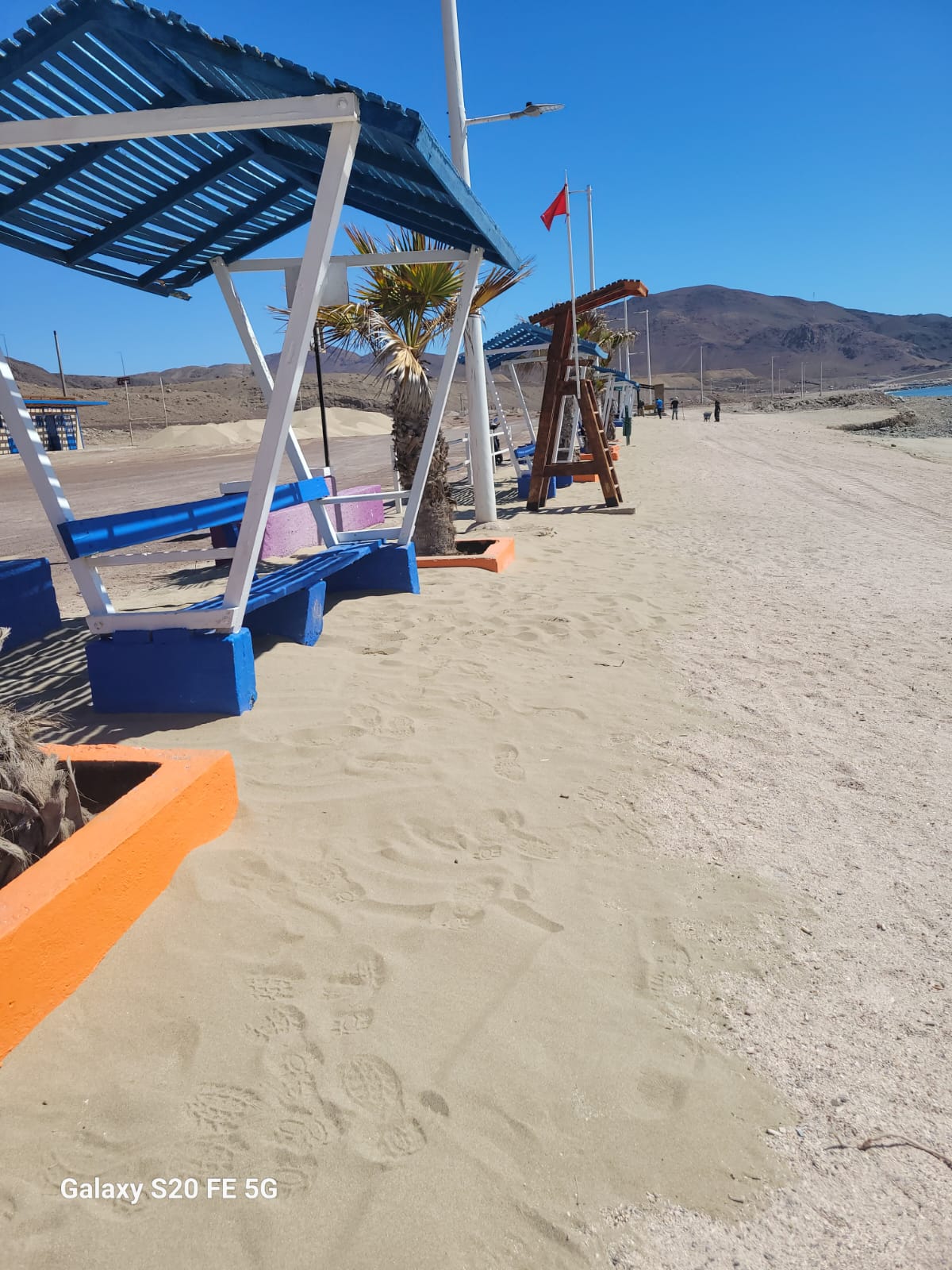 Vista de sombrillas azules y bancas recién pintadas en Playa Tierra del Moro, parte del programa de mantenimiento municipal en Taltal.