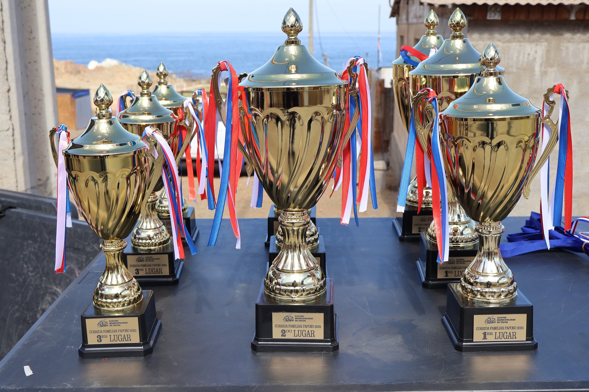Trofeos con cintas tricolores exhibidos junto al mar en la premiación de la Corrida Familiar Paposo 2025, destacando a ganadores de distintas categorías.