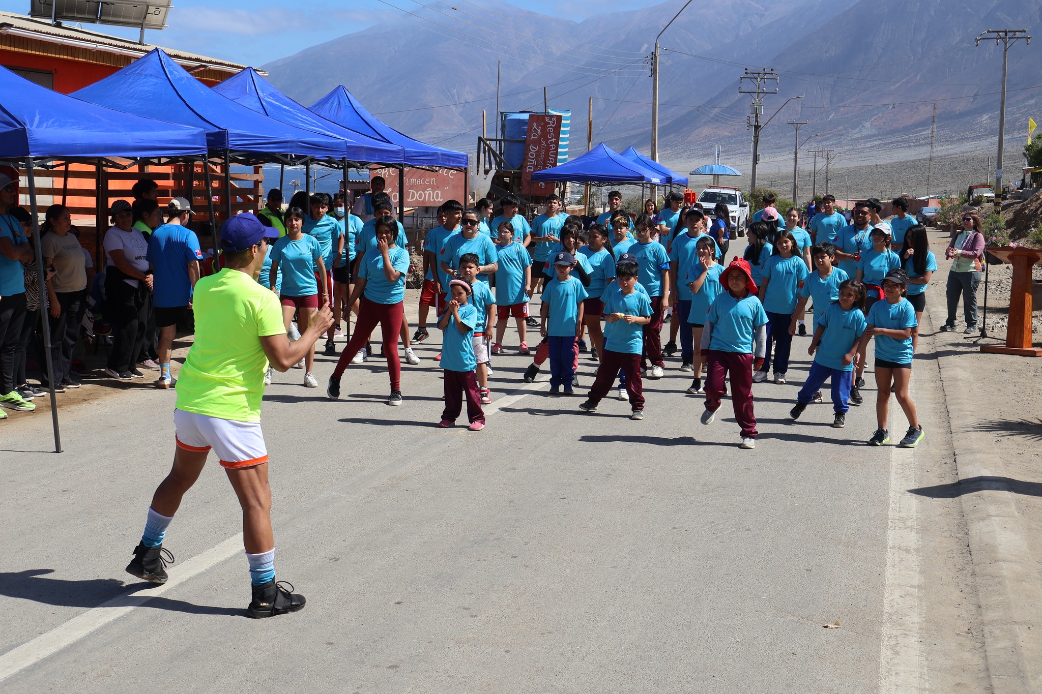 Decenas de vecinos y familias realizan ejercicios previos al inicio de la Corrida Familiar de Paposo 2025 en la avenida principal.