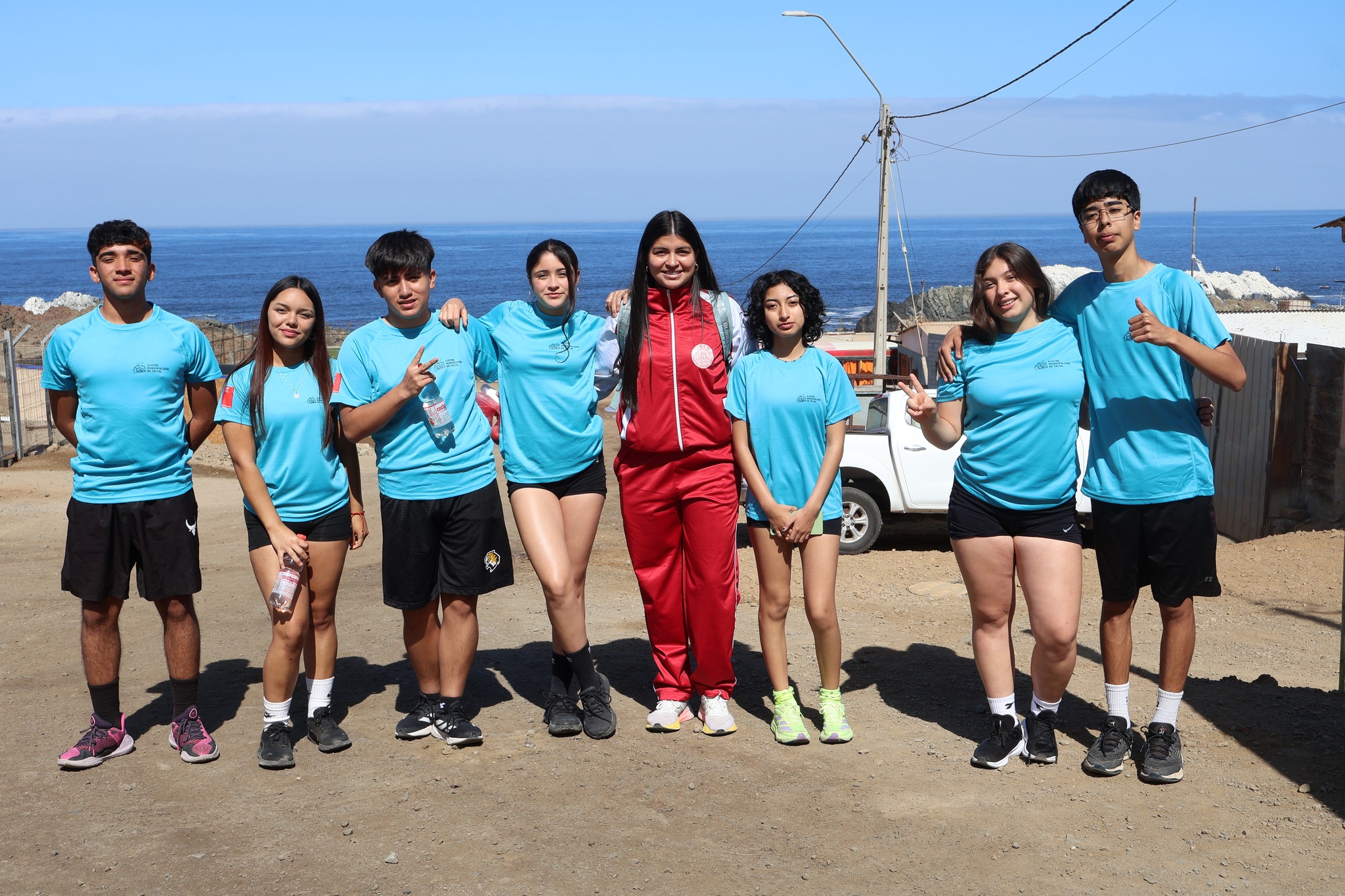 Grupo juvenil posa frente al mar tras participar en la Corrida Familiar de Paposo 2025, vistiendo poleras celestes institucionales.