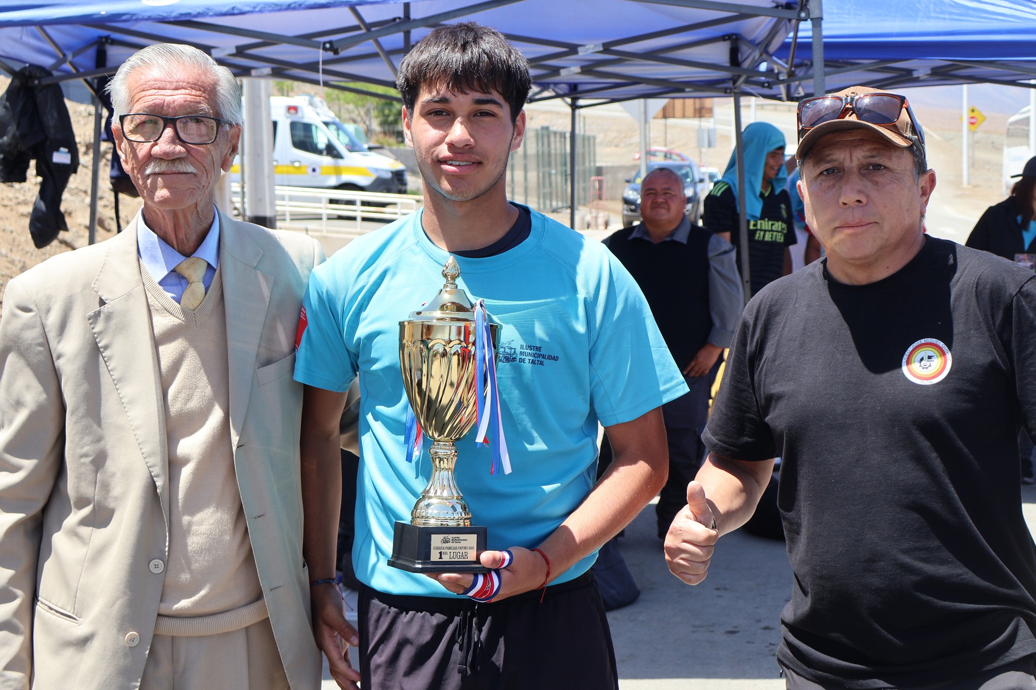 Joven ganador sostiene el trofeo del primer lugar acompañado por organizadores durante la Corrida Familiar de Paposo 2025.