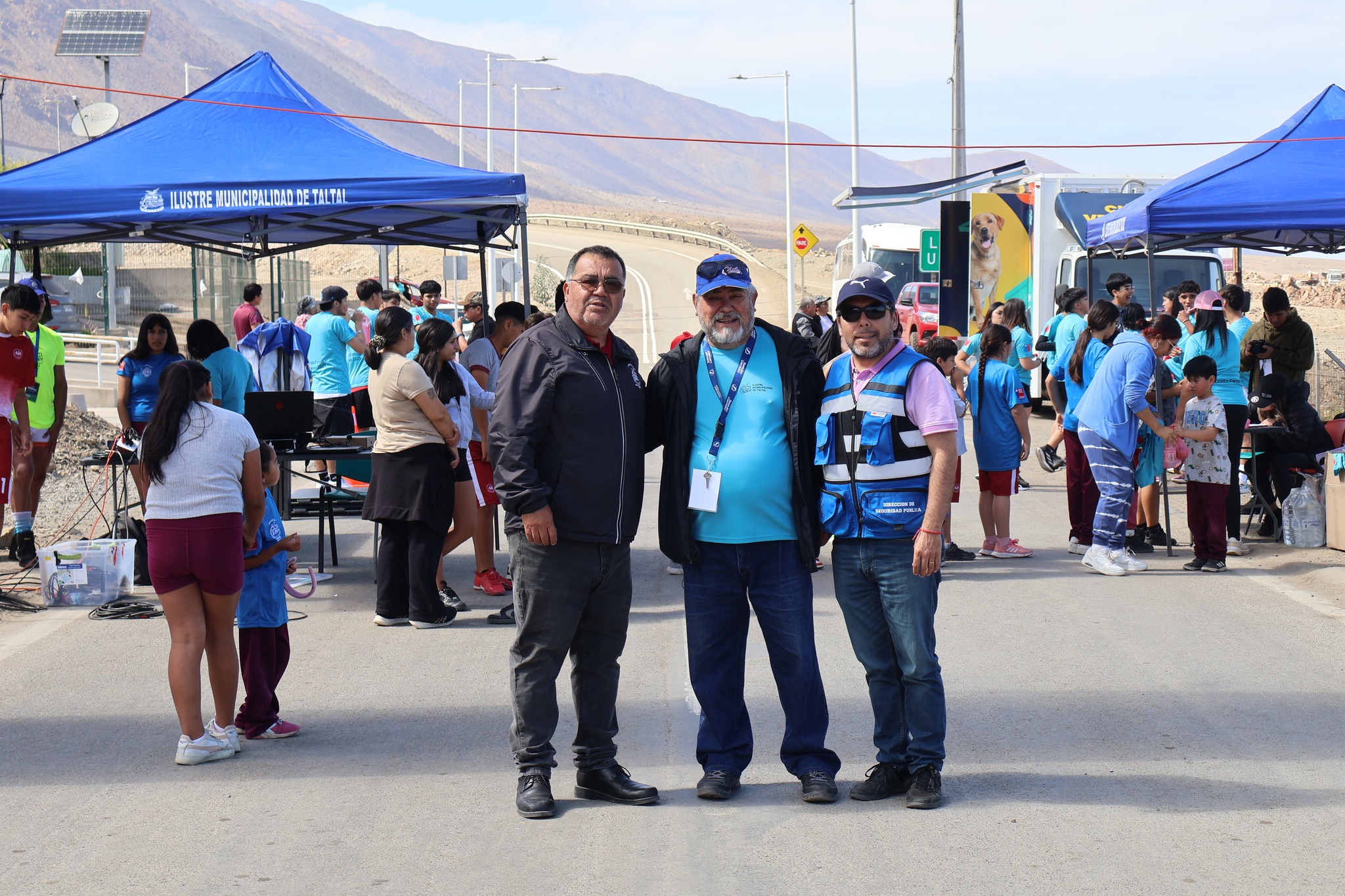 Autoridades municipales y equipo organizador posan durante la Corrida Familiar de Paposo 2025, junto a stands y carpas de apoyo logístico.